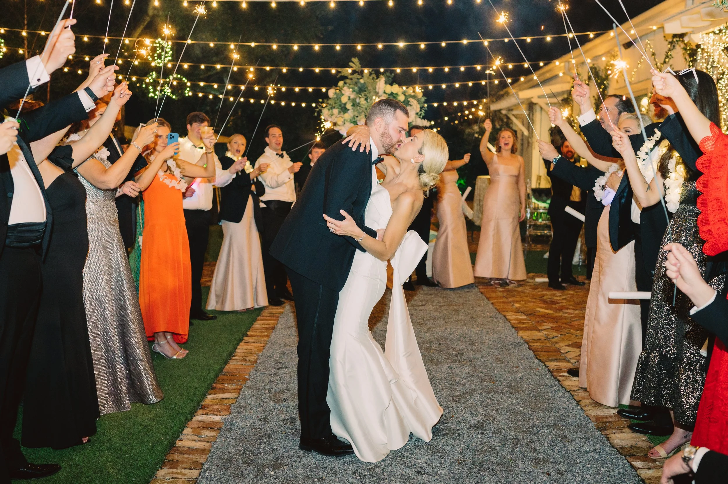 A bride and groom share a kiss during their wedding reception, surrounded by friends and family holding sparklers
