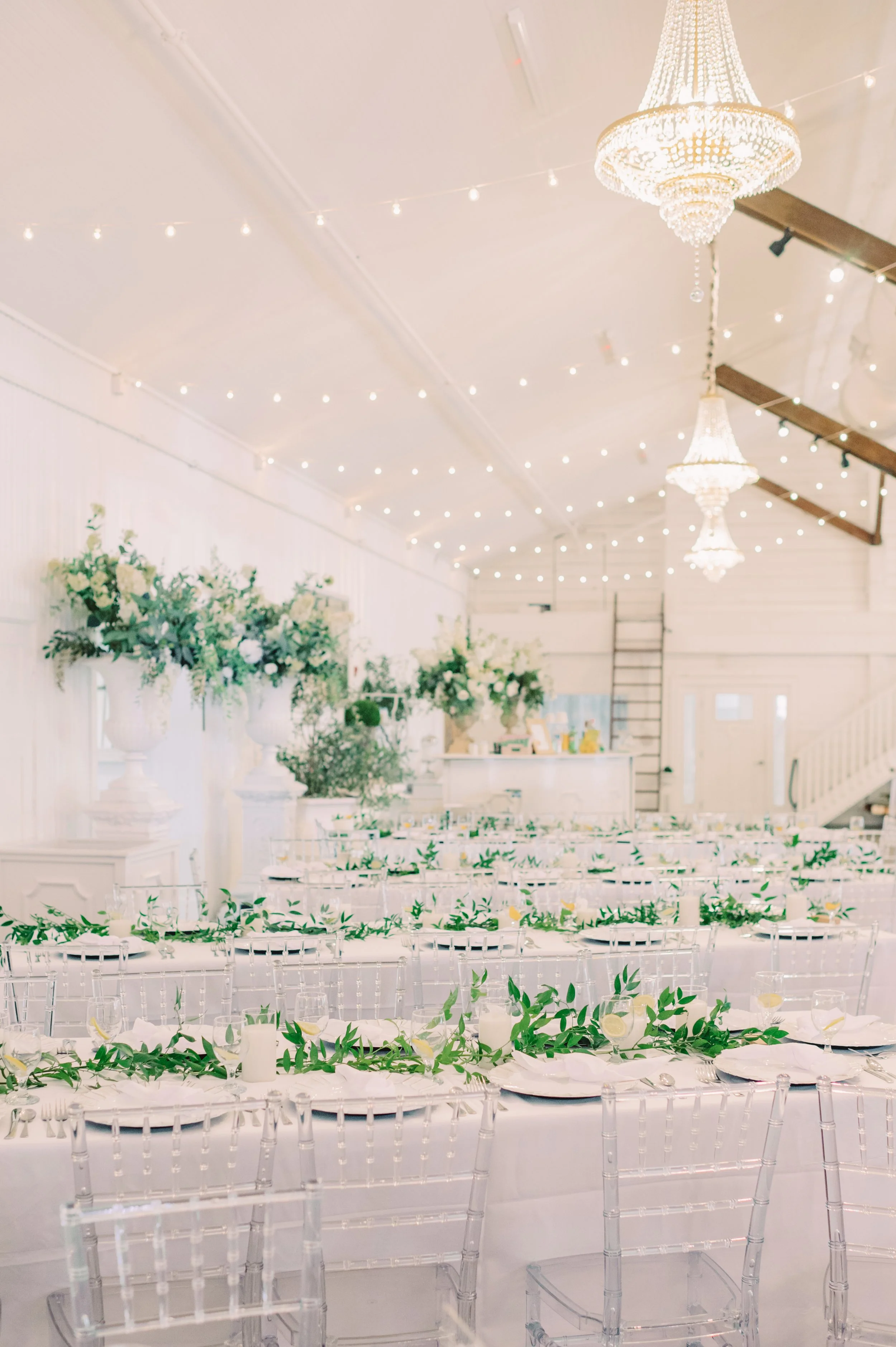 Decorated banquet hall with long tables, floral centerpieces, and chandeliers hanging from the ceiling.