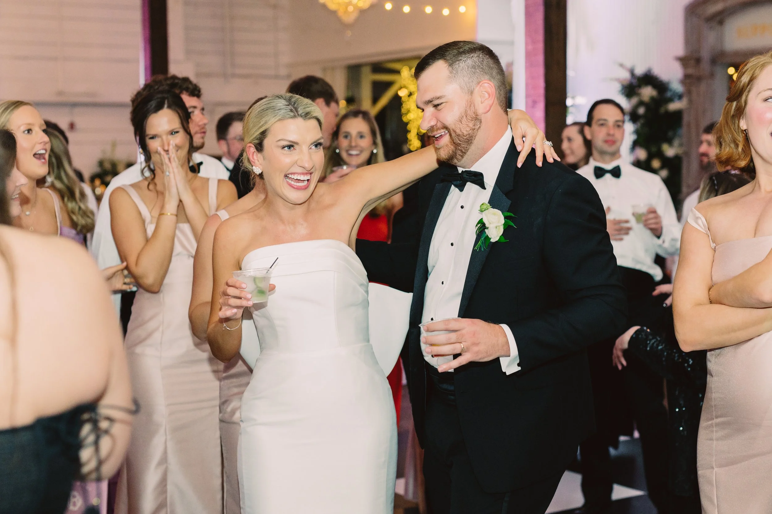 A wedding reception with a bride and groom dancing and smiling, surrounded by guests dressed in formal attire.