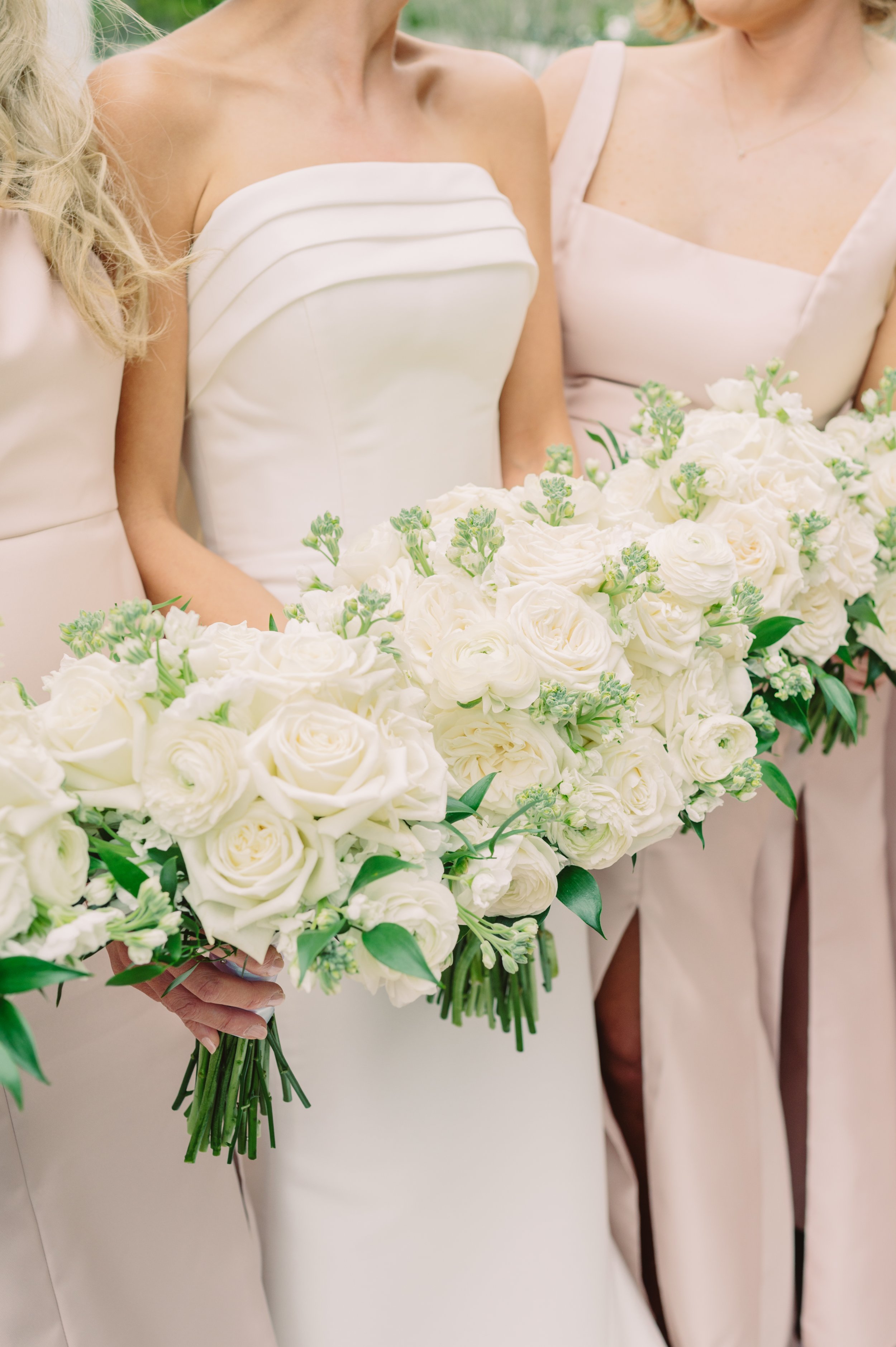 A bride and bridesmaids holding a large bouquet of white roses and flowers at a wedding.