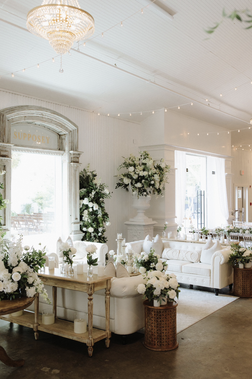Elegant, white-decorated wedding or event venue with floral arrangements, sofas, candles, and soft lighting in a Pensacola Wedding Venue.