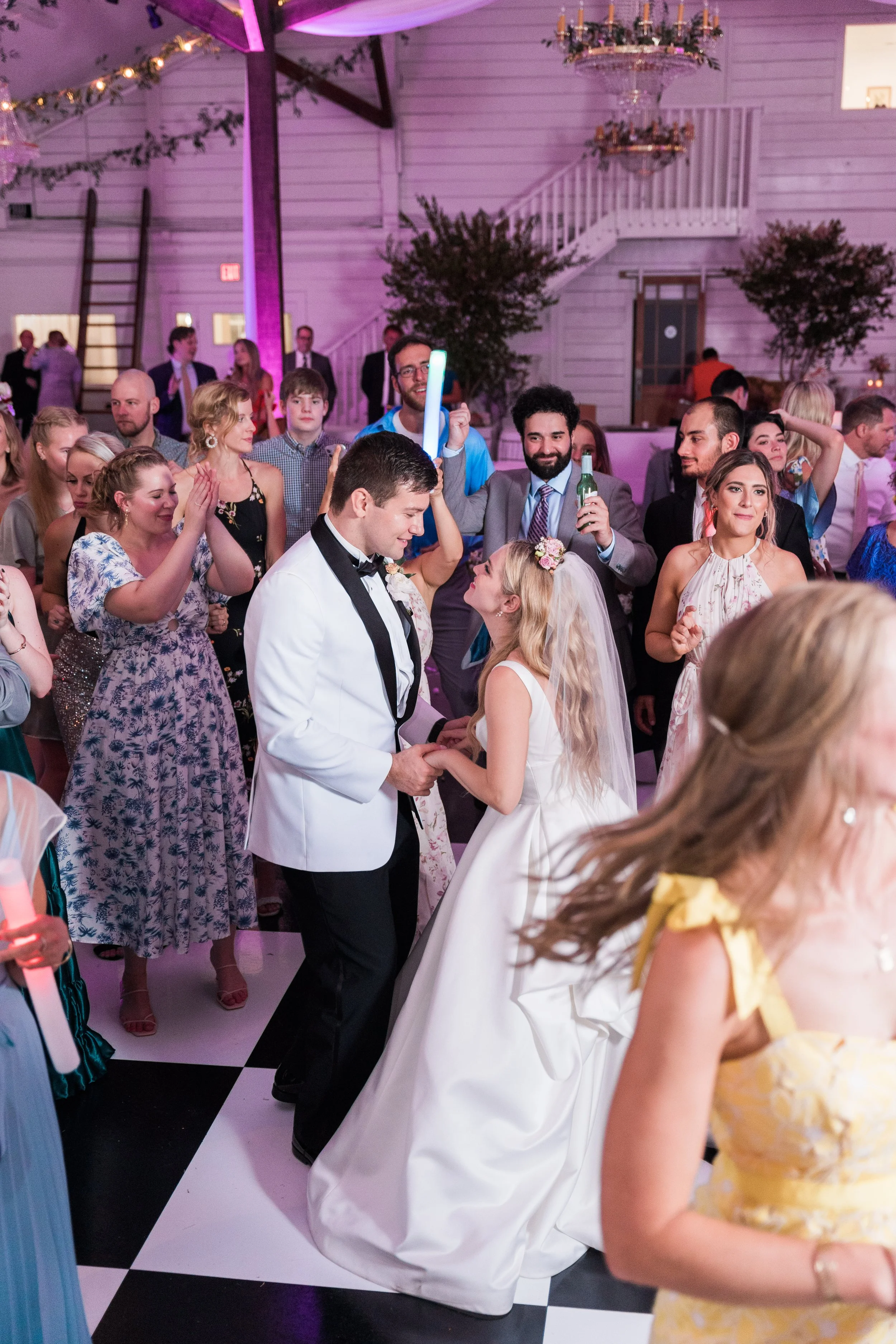 A Pensacola Wedding reception with bride and groom dancing surrounded by guests, colorful lighting, and festive decorations.