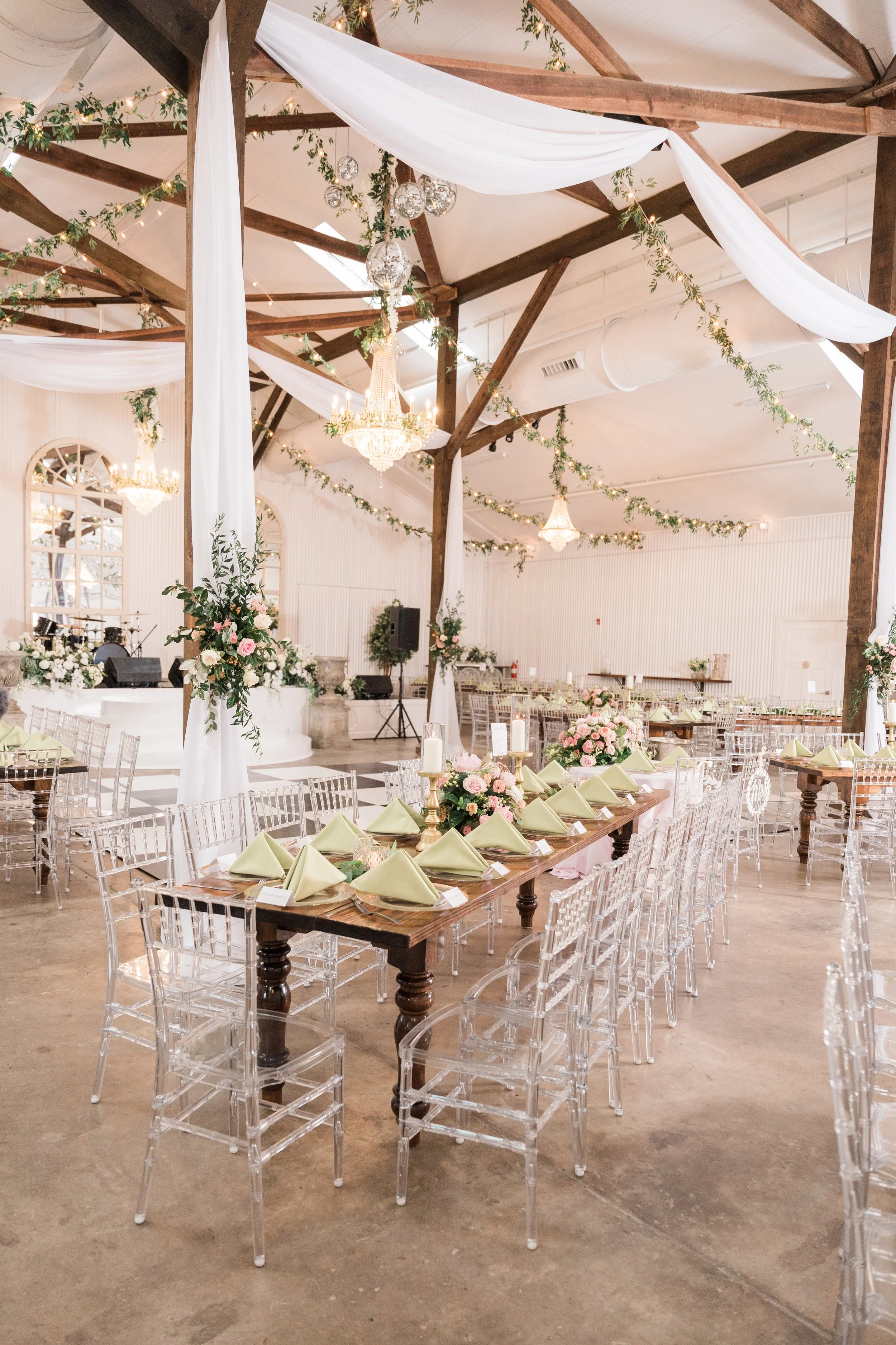 A decorated event space with tables and chairs, chandeliers, and draped fabrics on the ceiling, suitable for a wedding or celebration in Pensacola.