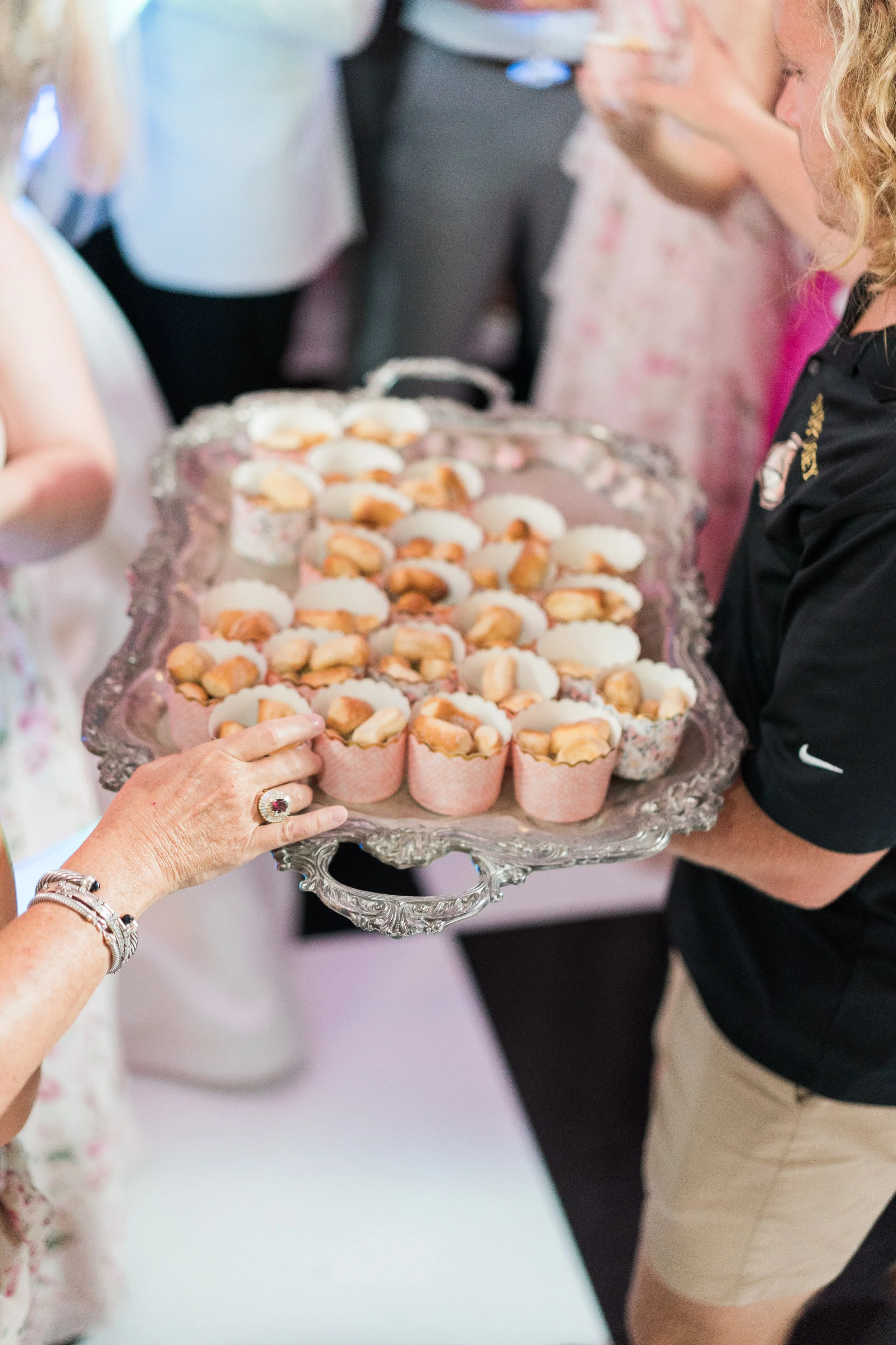 A person holding a large ornate silver tray filled with mini cupcakes at a social gathering.