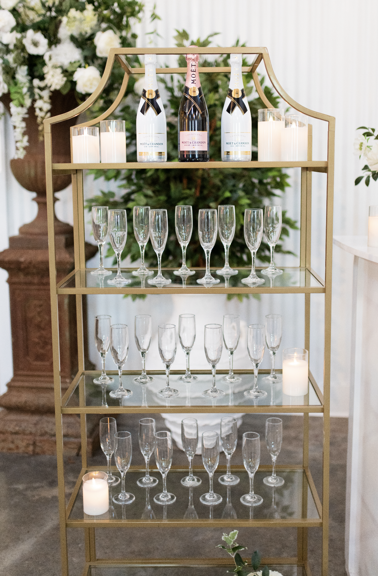 Elegant gold champagne cart with bottles of Moët & Chandon champagne on top, surrounded by candles and empty champagne flutes, with floral arrangements in the background.