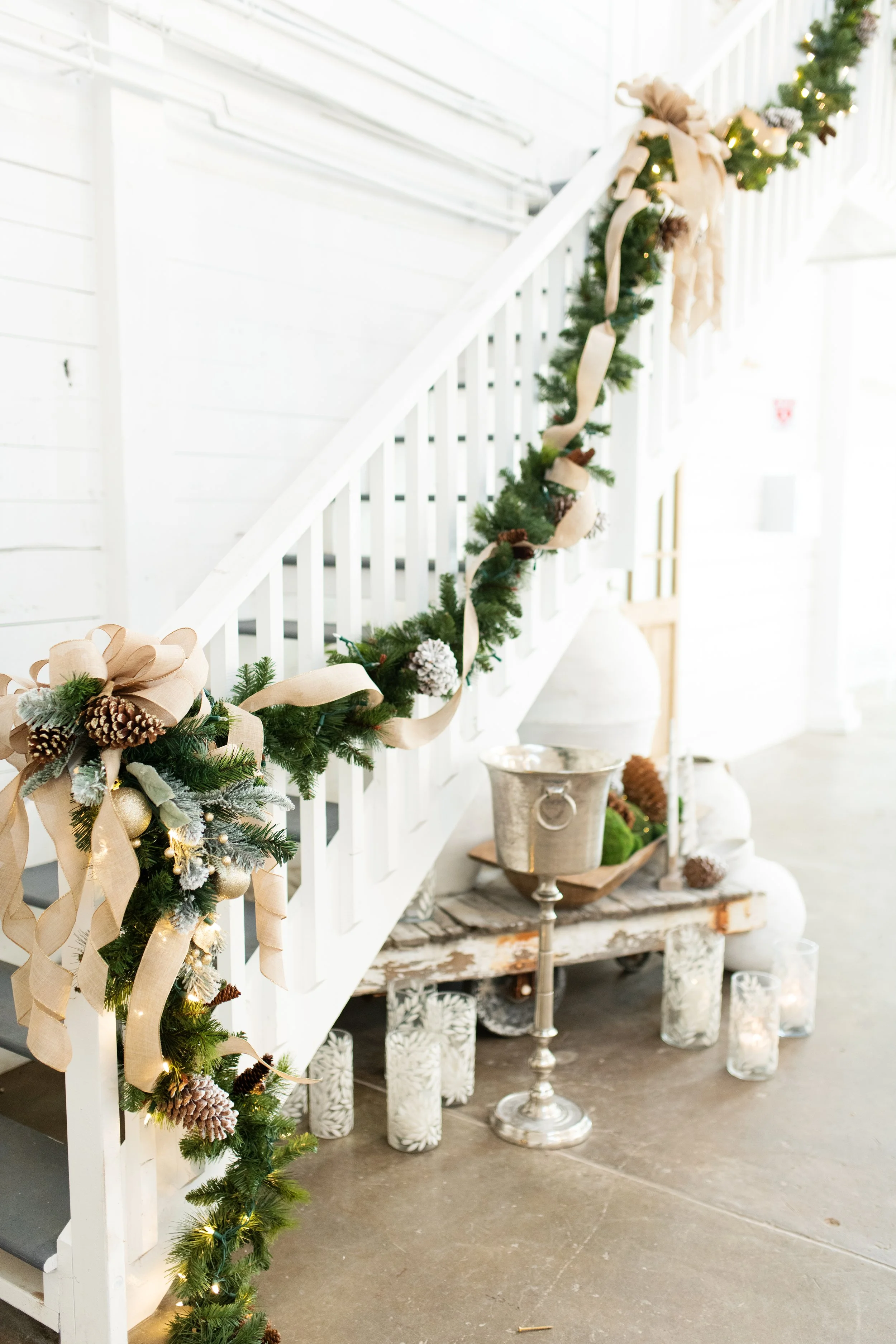 Decorated staircase with green garland, beige ribbons, pinecones, and fairy lights, with holiday decorations and candles below in a Pensacola Wedding Venue.