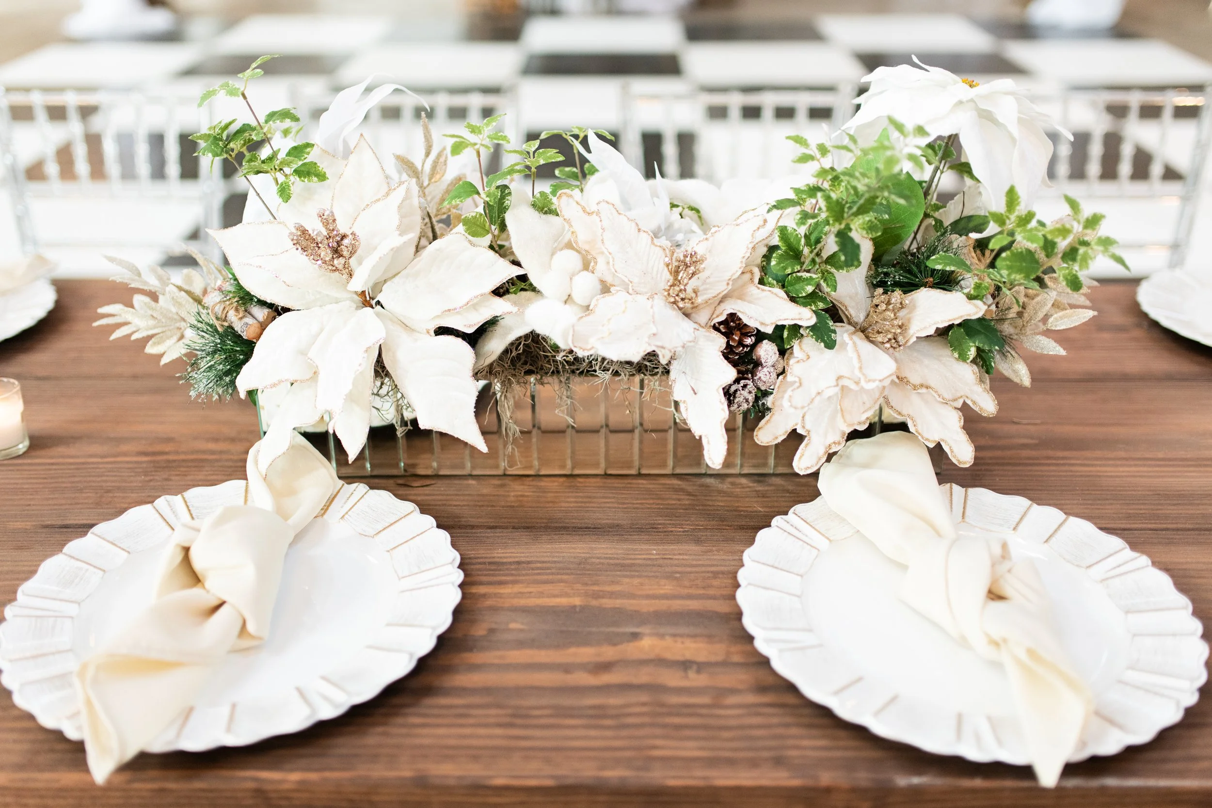 Table centerpiece with white poinsettias, greenery, pinecones, and decorative berries in a Pensacola Wedding Venue.