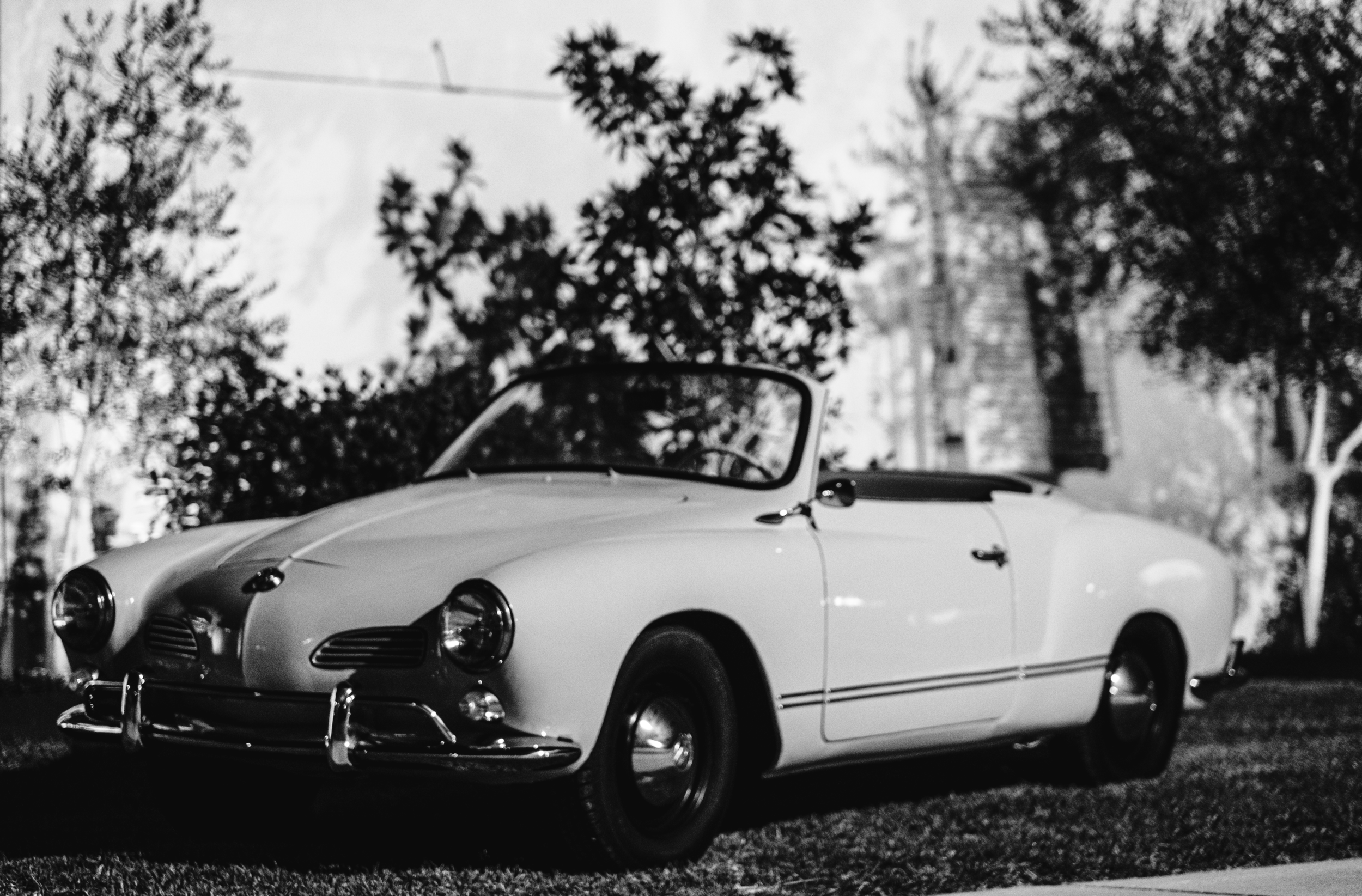 A vintage white convertible car parked on a grassy area of a Pensacola Wedding Venue with trees and power lines in the background.