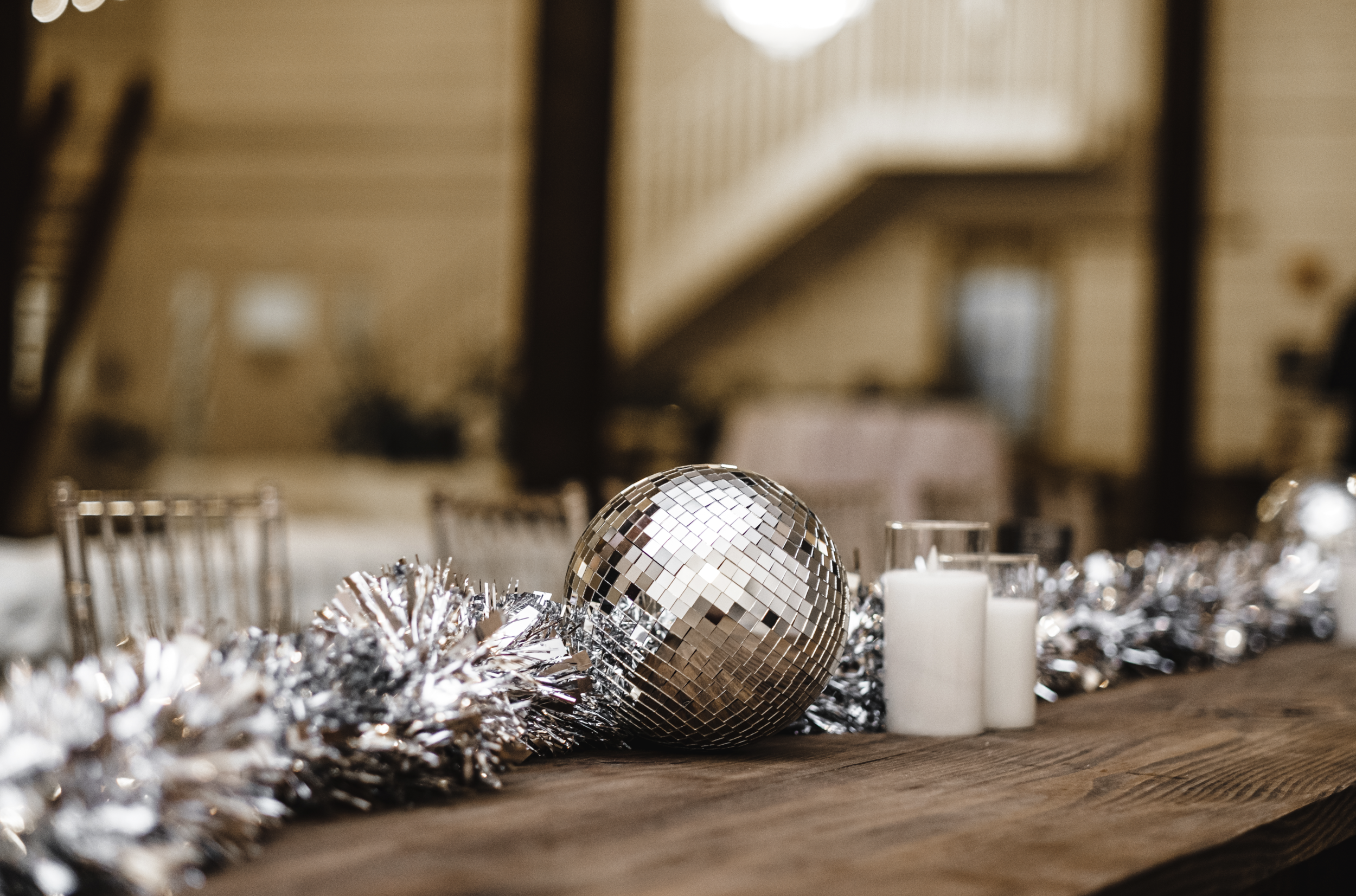 Decorative Christmas table centerpiece with silver disco ball, white candles, and silver tinsel on a wooden table in a rustic setting in a Pensacola Wedding Venue.