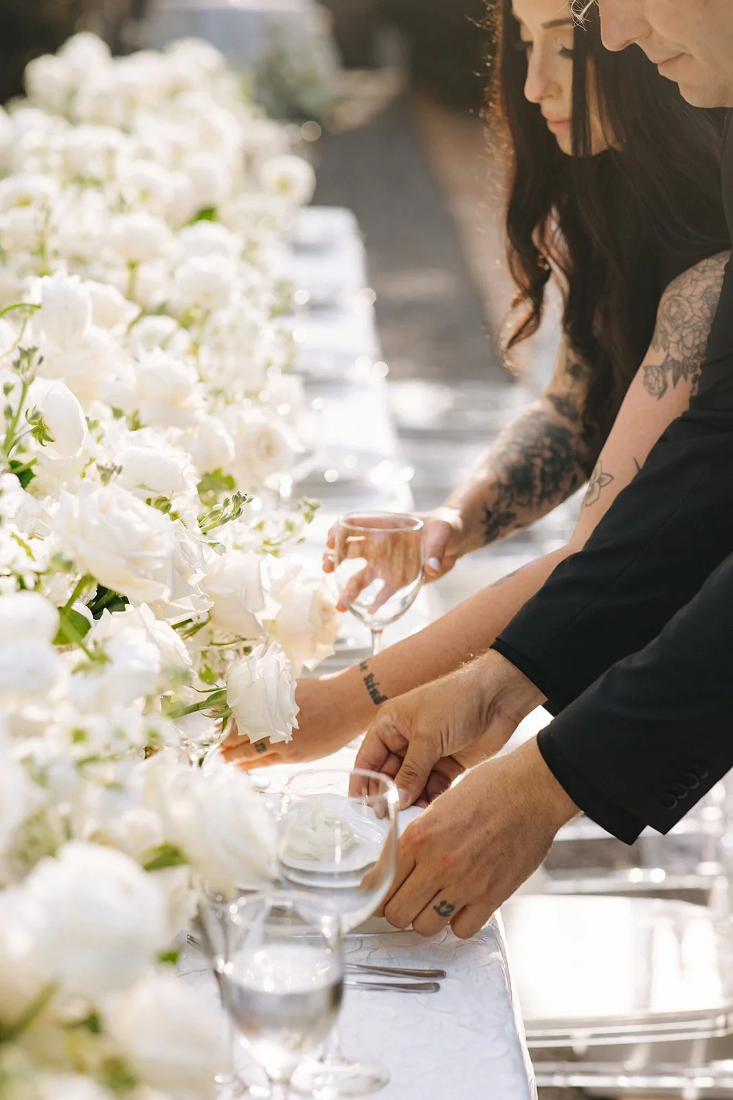 A Pensacola Wedding Venue owner setting a formal table with white flowers, glassware, and utensils outdoors in sunlight.