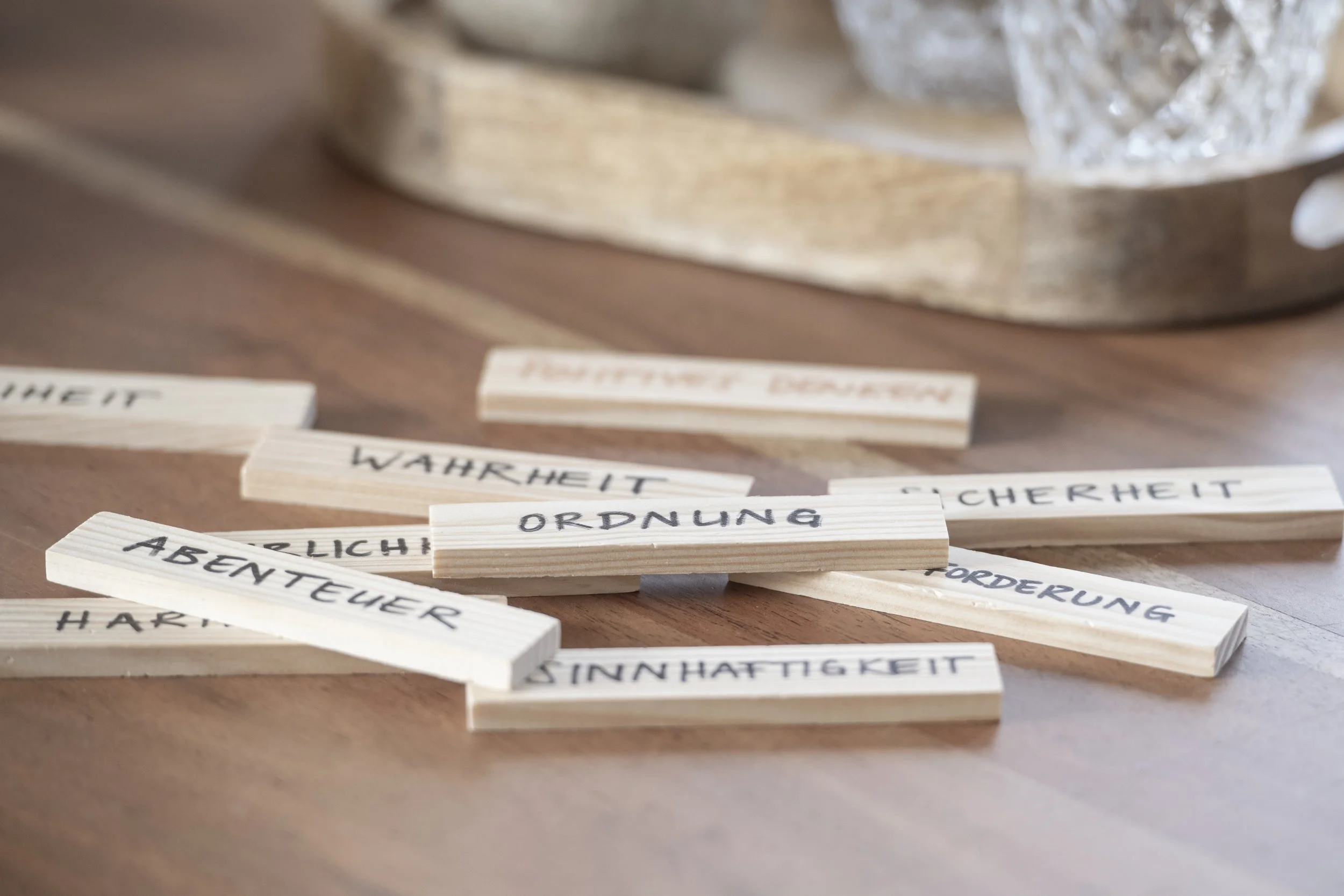 Holzbuchstaben mit deutschen Begriffen wie 'Wahrheit', 'Ordnung', 'Abenteurer' und andere, die auf einem Holz- oder Tischoberfläche liegen.