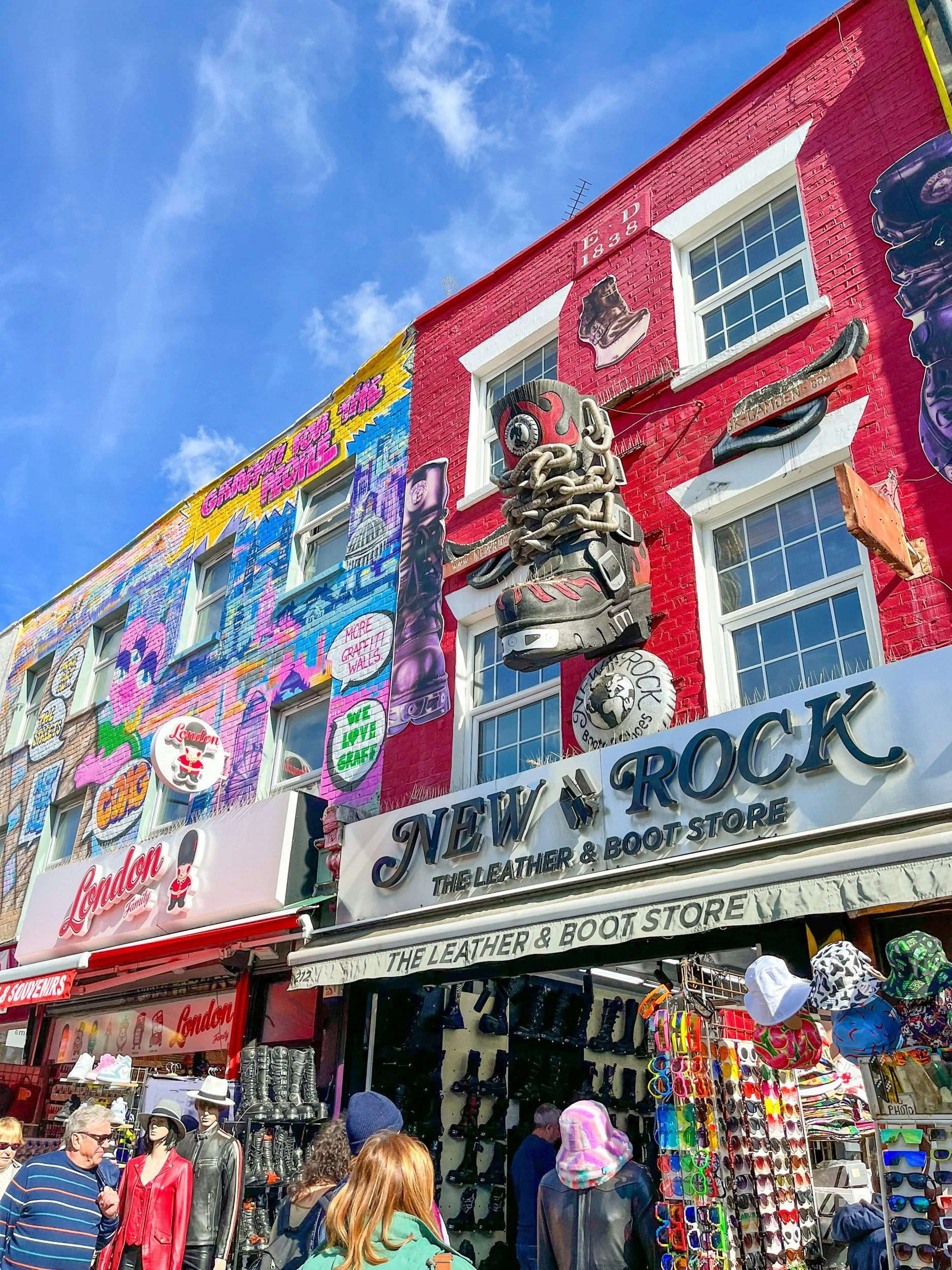 Central Victorian House | Camden Town | People shopping at an outdoor market with a store sign for 'New & Rock, The Leather & Boot Store,' colorful murals on the building, mannequins dressed in leather jackets, and hats and sunglasses for sale.