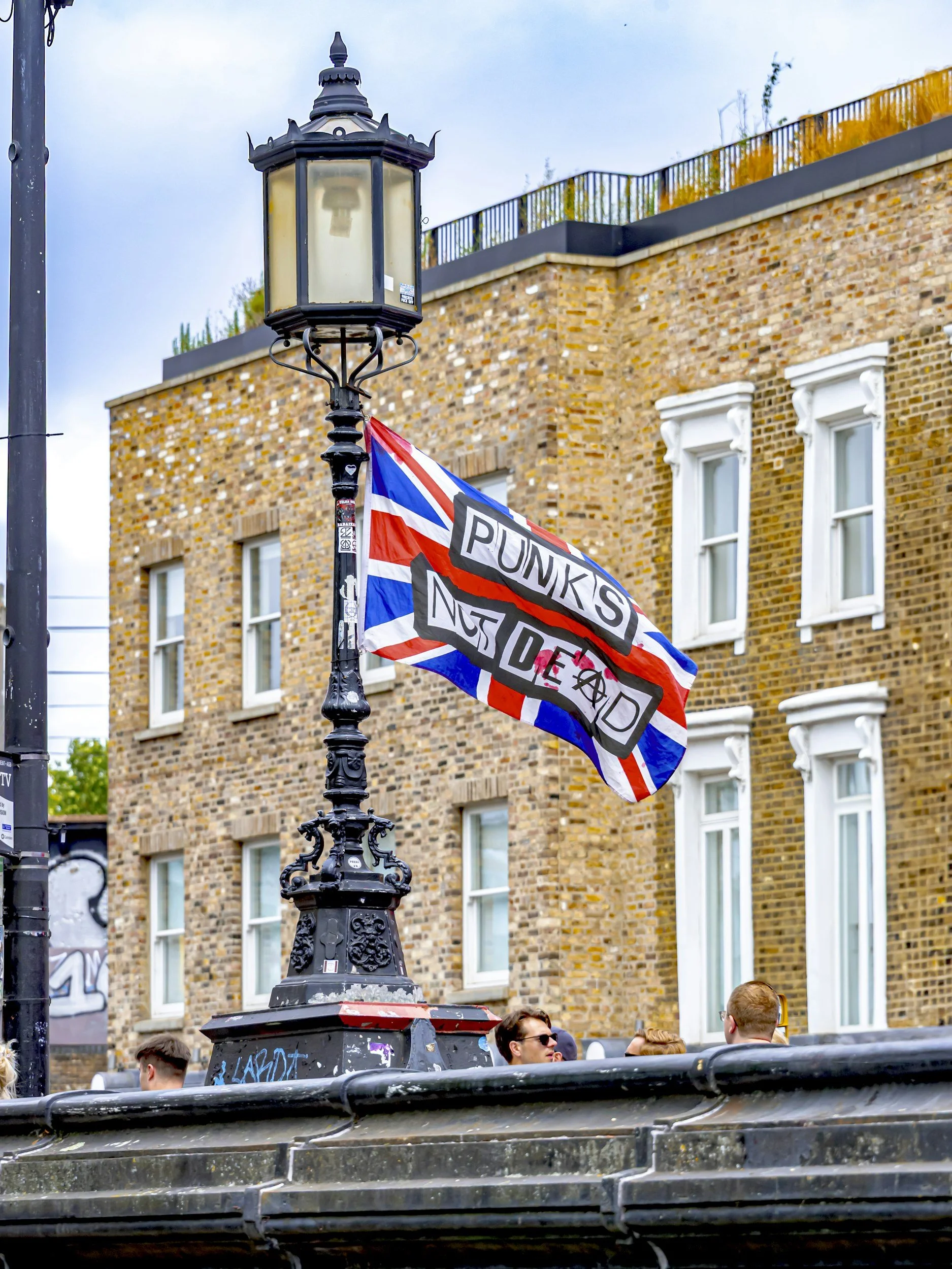 Central Victorian House | Camden Town | Street scene with vintage black lamppost, union jack flag with message 'Punks Not Dead' attached, and people walking in front of a brick building with white window frames.