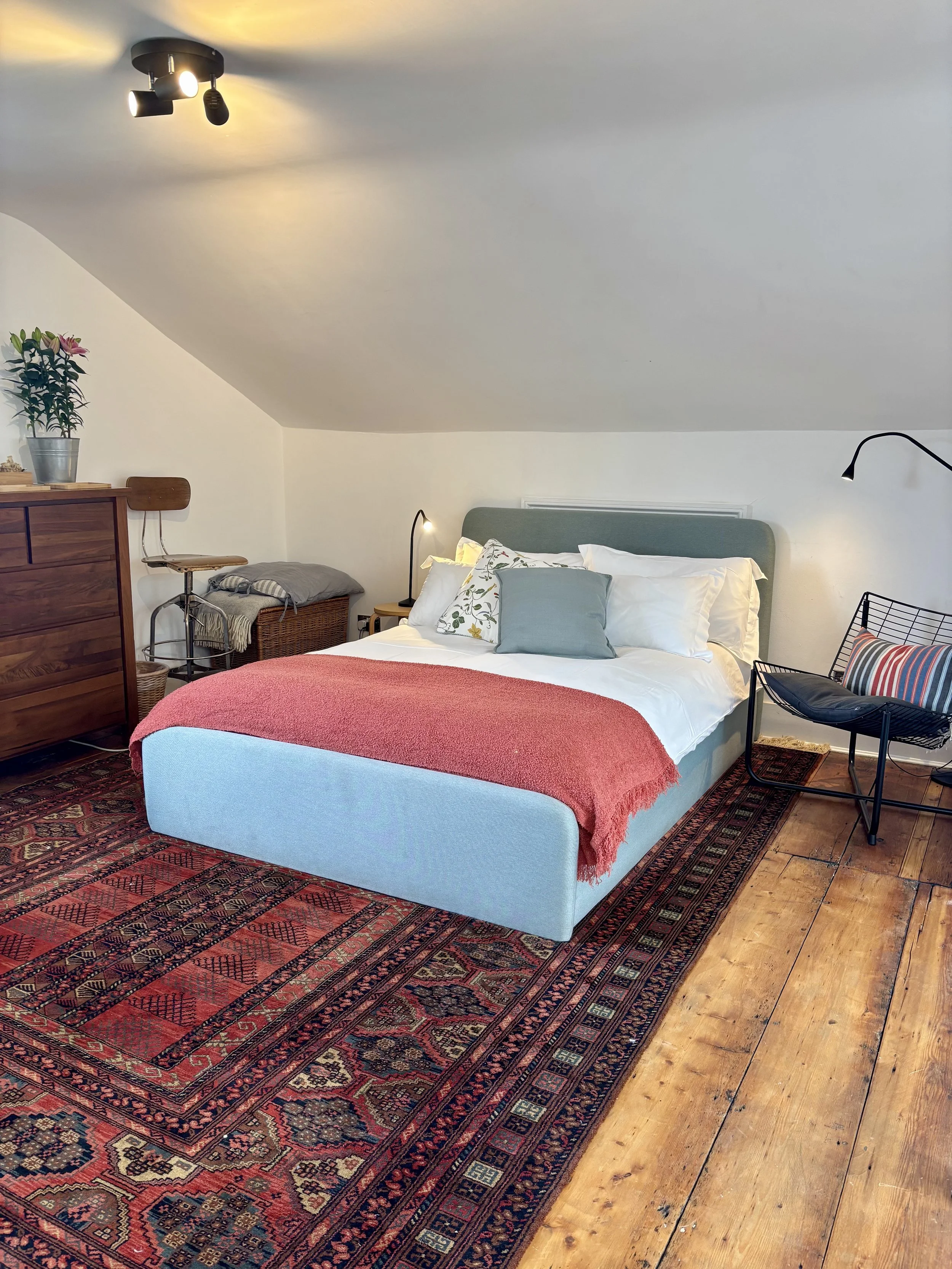 A cozy bedroom with a bed, an area rug, a chair, a dresser, and various lamps.