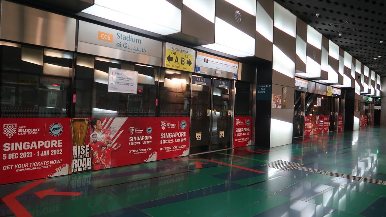 Empty airport terminal with glass doors, illuminated ceiling panels, and promotional banners for the AFC Suzuki Cup 2020.