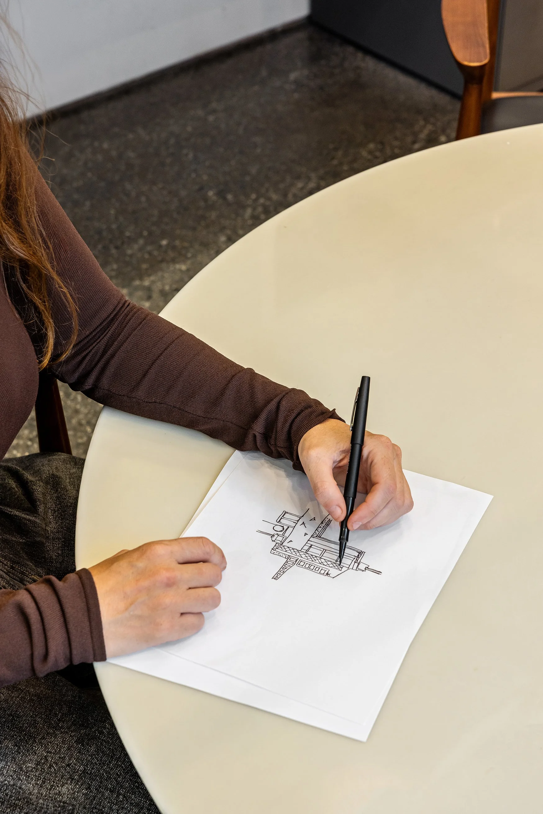 A person with brown long sleeve shirt drawing or working on architectural plans or blueprints at a white table.
