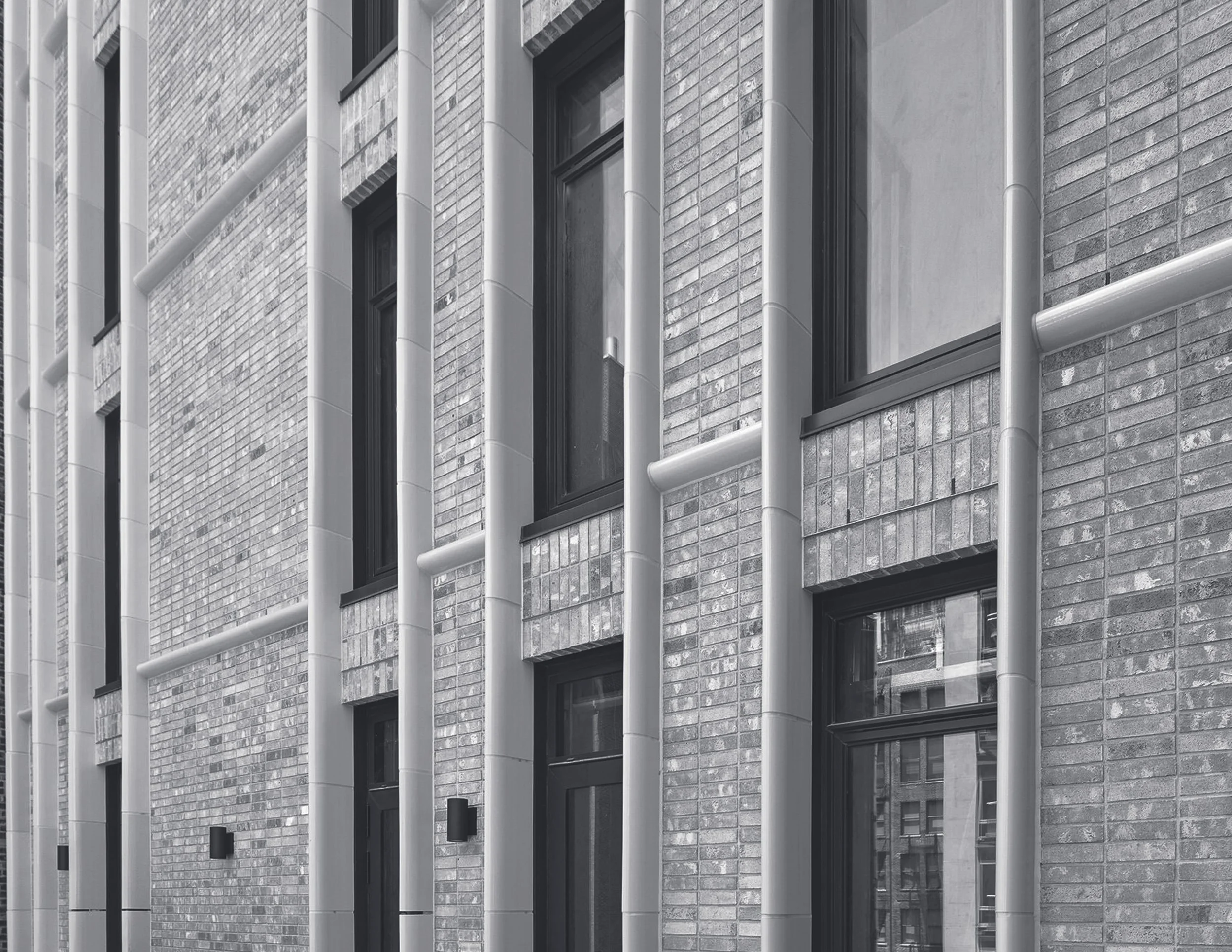 Gray brick building with black-framed windows and white vertical pipes running along the facade.