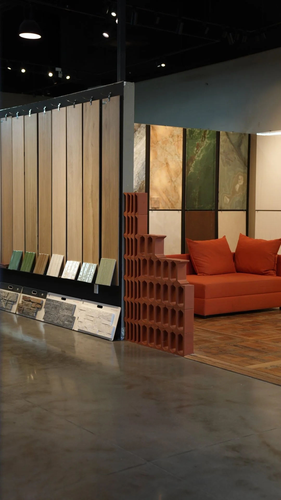Interior of a showroom displaying various types of wall tiles, flooring samples, and decorative materials with a cozy orange sofa in the background.