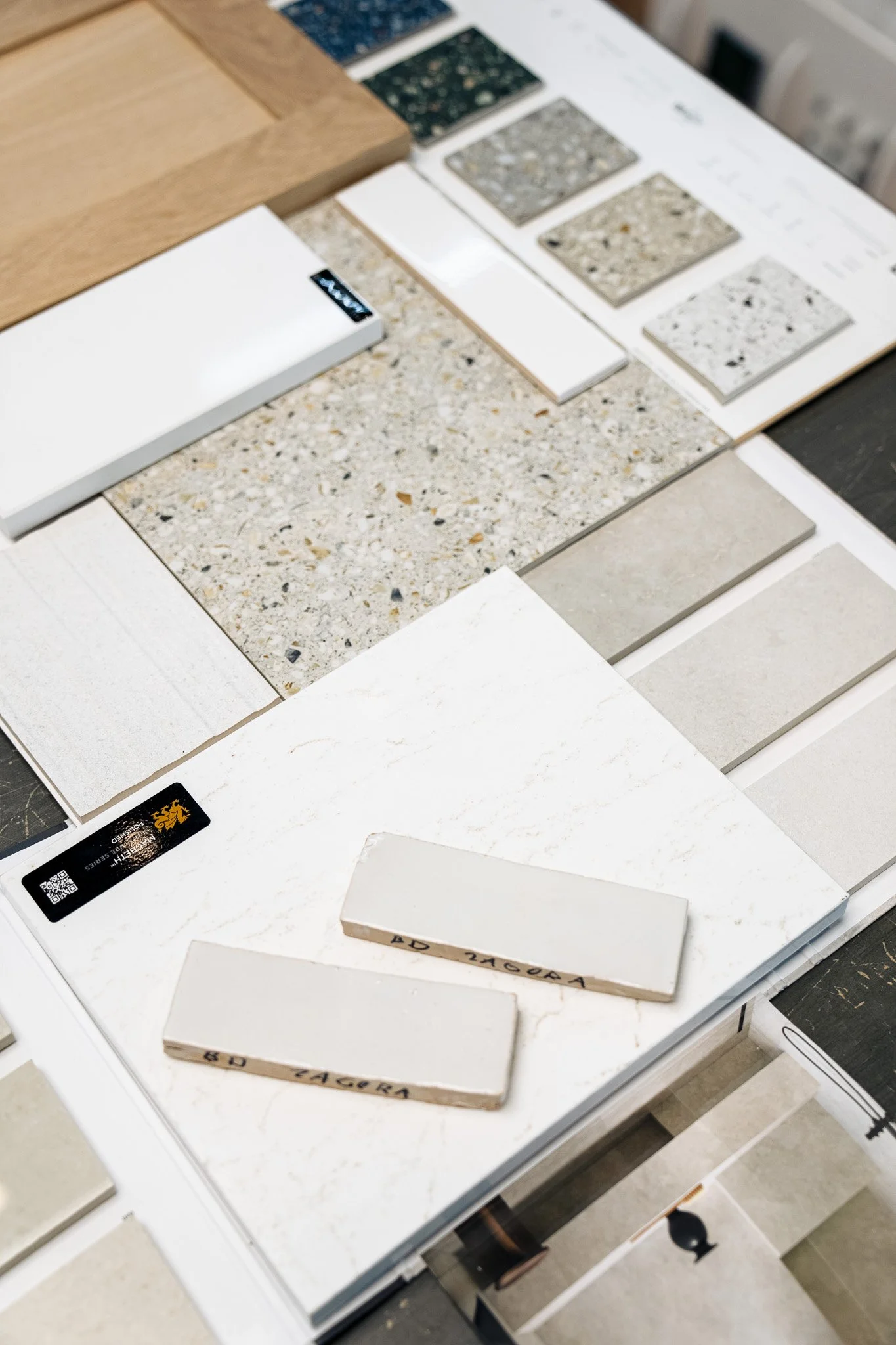 Display of various countertop sample tiles in different colors and textures, arranged on a white table, with some wooden samples and labels visible.