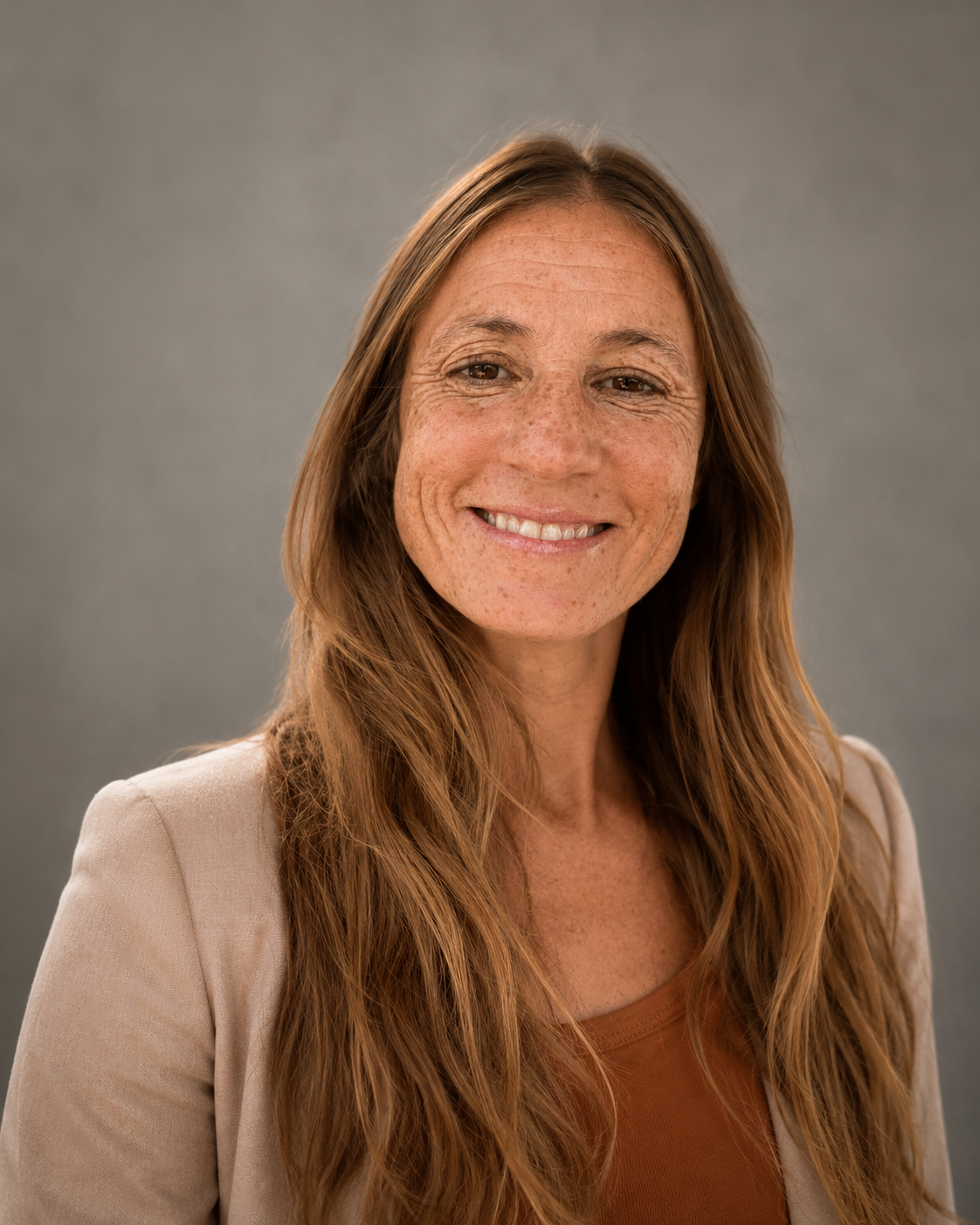A woman with long reddish-brown hair, smiling, against a plain gray background.