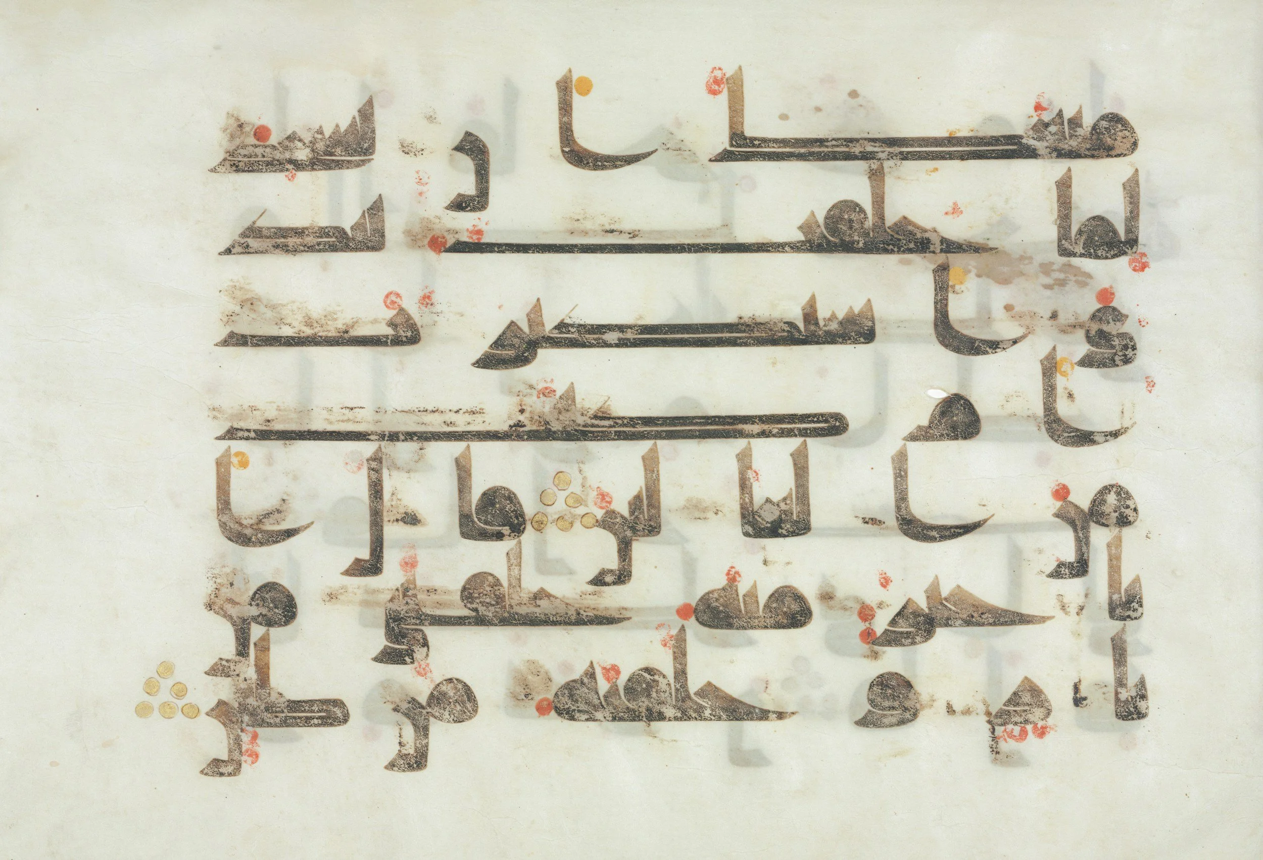 Close-up of ancient Arabic calligraphy inscription with weathered appearance, ink stains, and red, yellow, and white paint splatters on a light background.