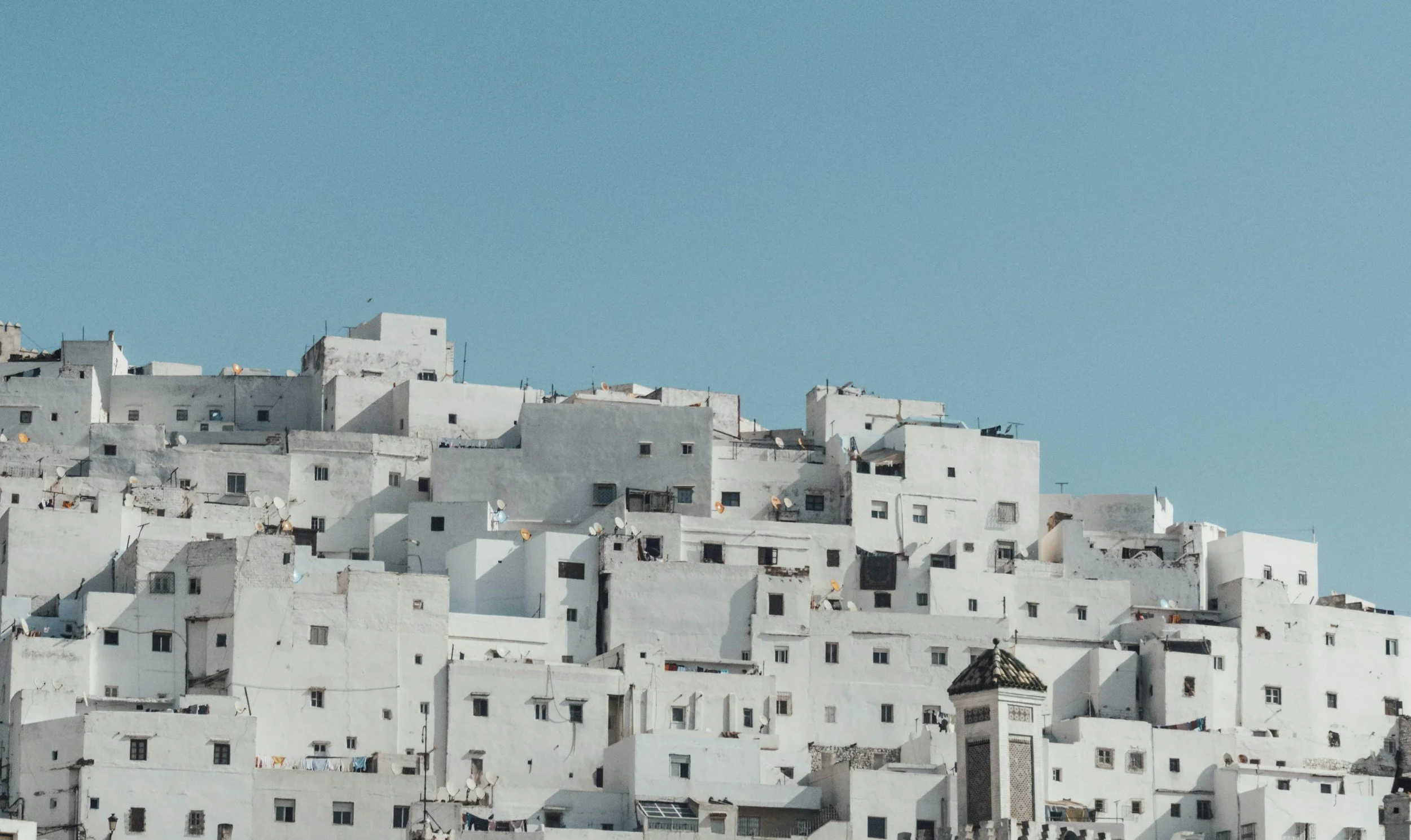 A hillside town with numerous white buildings stacked closely together under a clear blue sky.