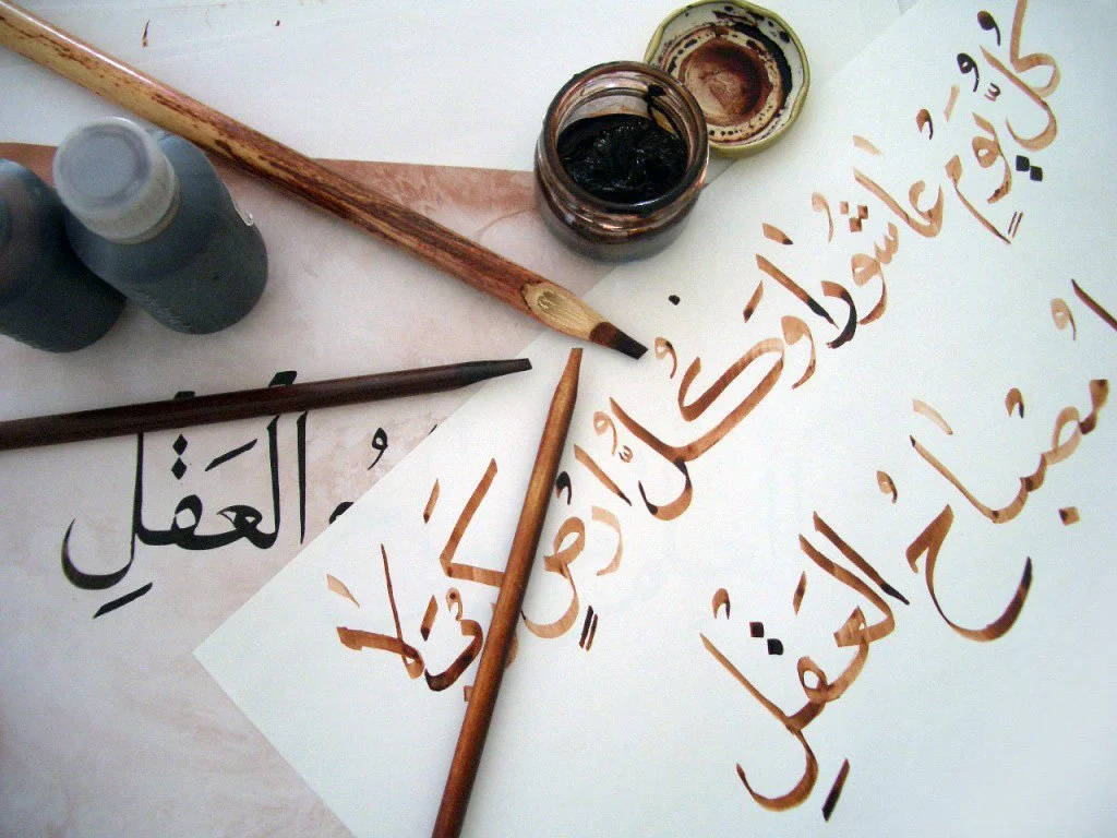 Arabic calligraphy art supplies including brushes, ink, and paper with Arabic script.
