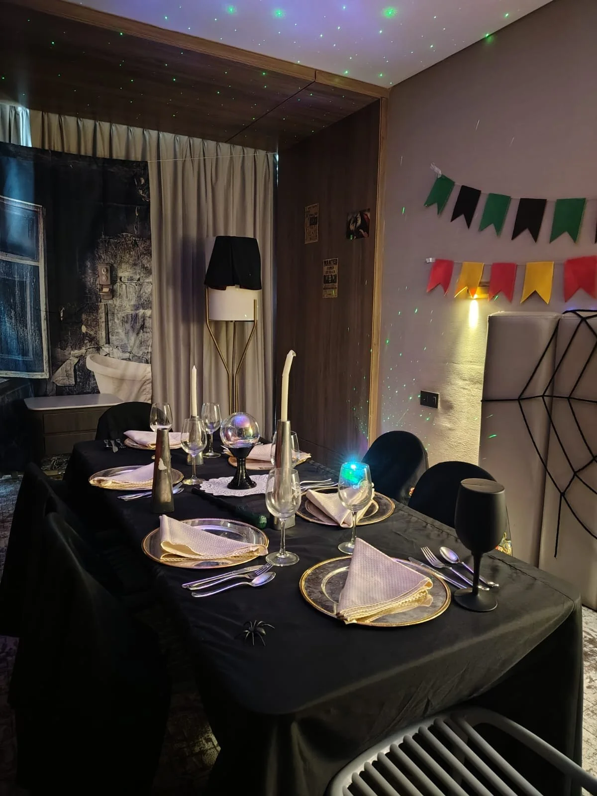 Mesa decorada para una celebración con copas, platos y servilletas doradas, en una habitación con decoraciones de fiesta y luces de colores.