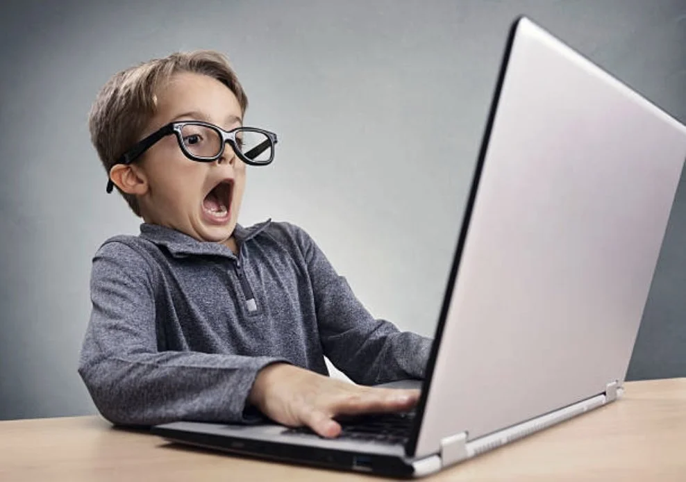A young boy with glasses looking surprised at his open laptop when he sees his diagnosis of chronic Lyme disease.