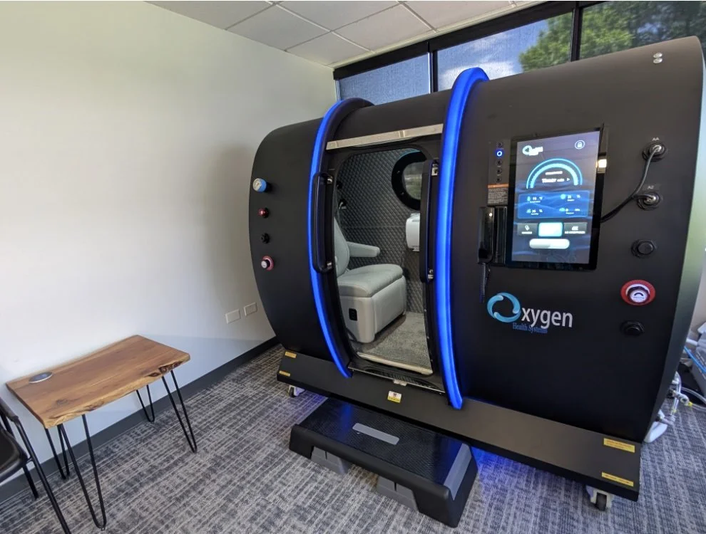 Hyperbaric oxygen therapy chamber with a reclining chair inside, in a medical facility.