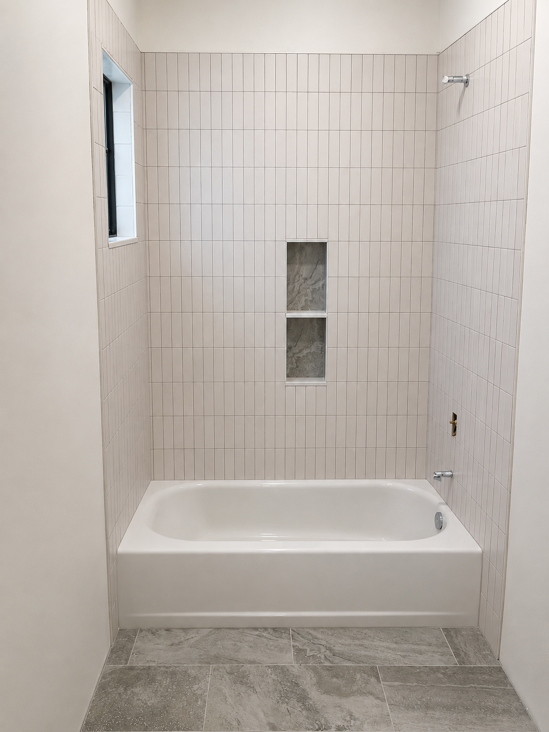 Bathroom bathtub with tiled walls, a window on the left, and a built-in niche in the center wall.