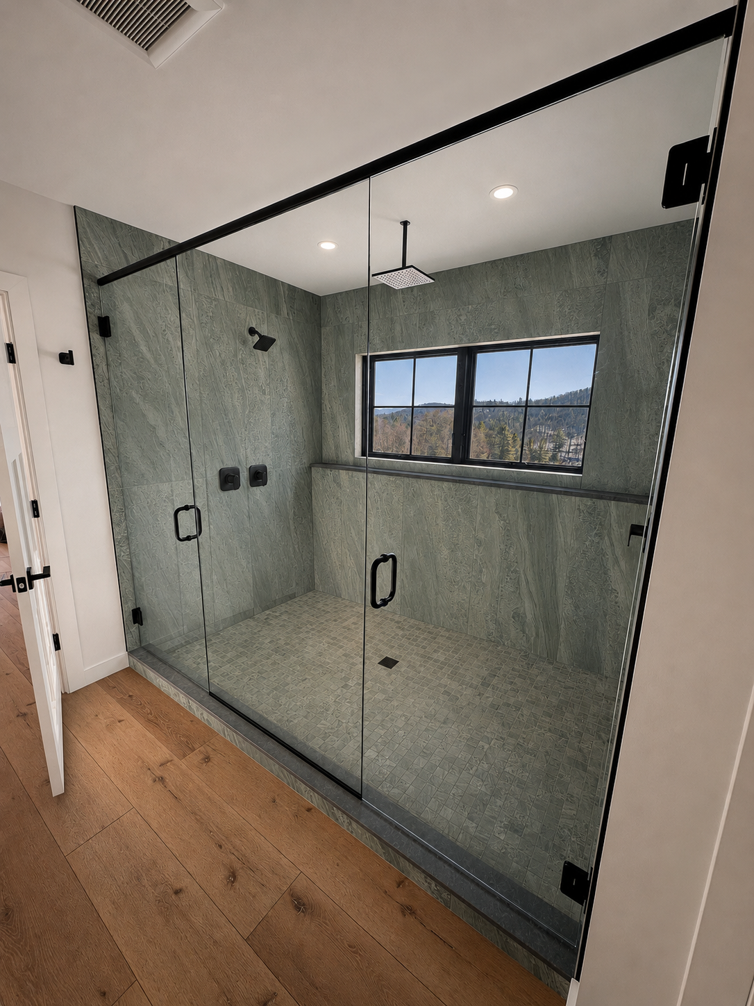Modern walk-in shower with glass doors, green marble walls, a window, rainfall showerhead, and two black controls inside