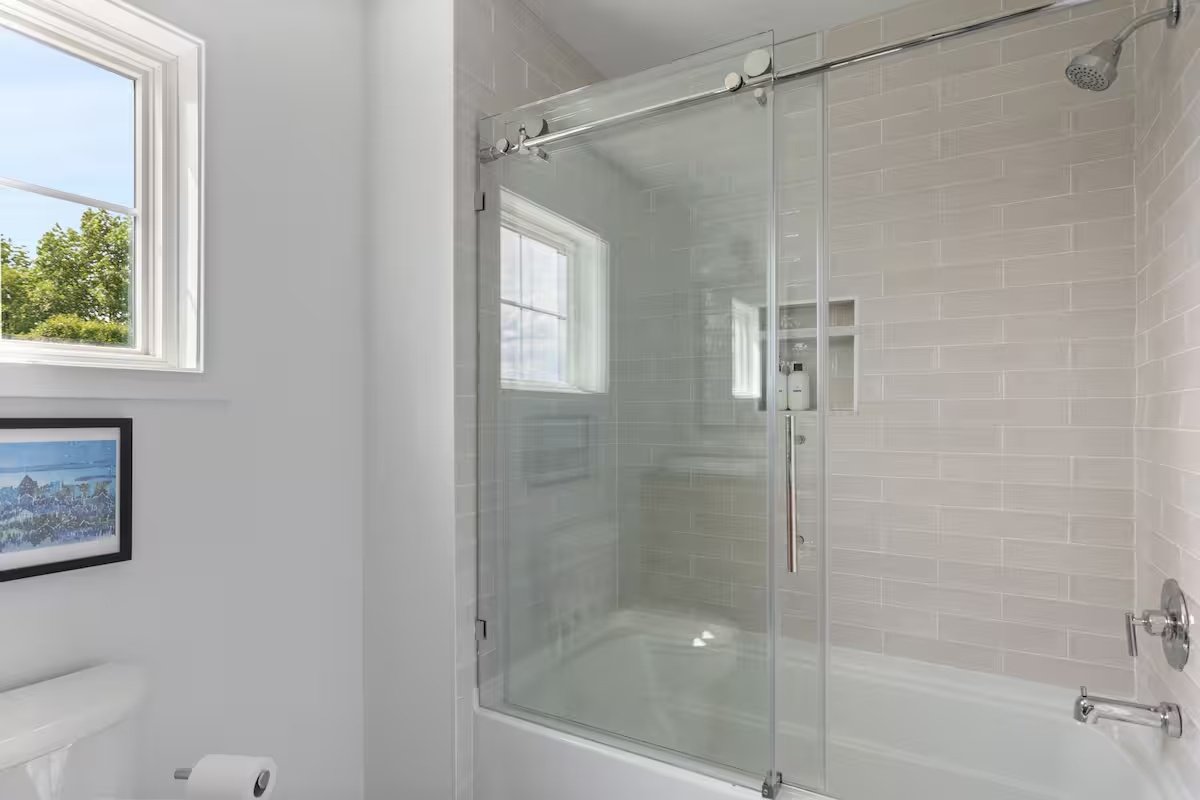 Bathroom with a glass-enclosed shower, a window, and a framed picture on the wall.