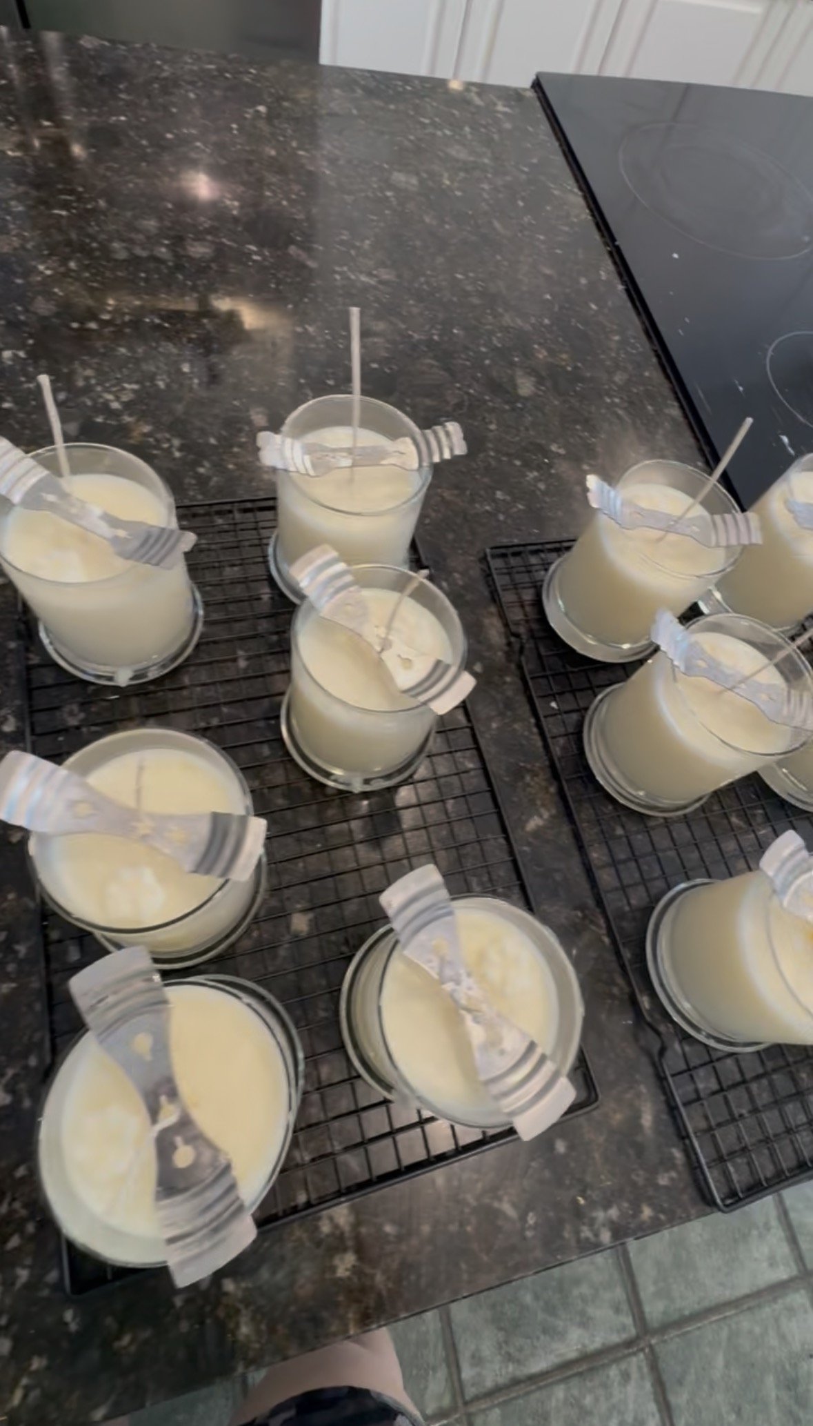 Several small cups of melted wax on cooling racks on a black granite countertop kitchen surface.