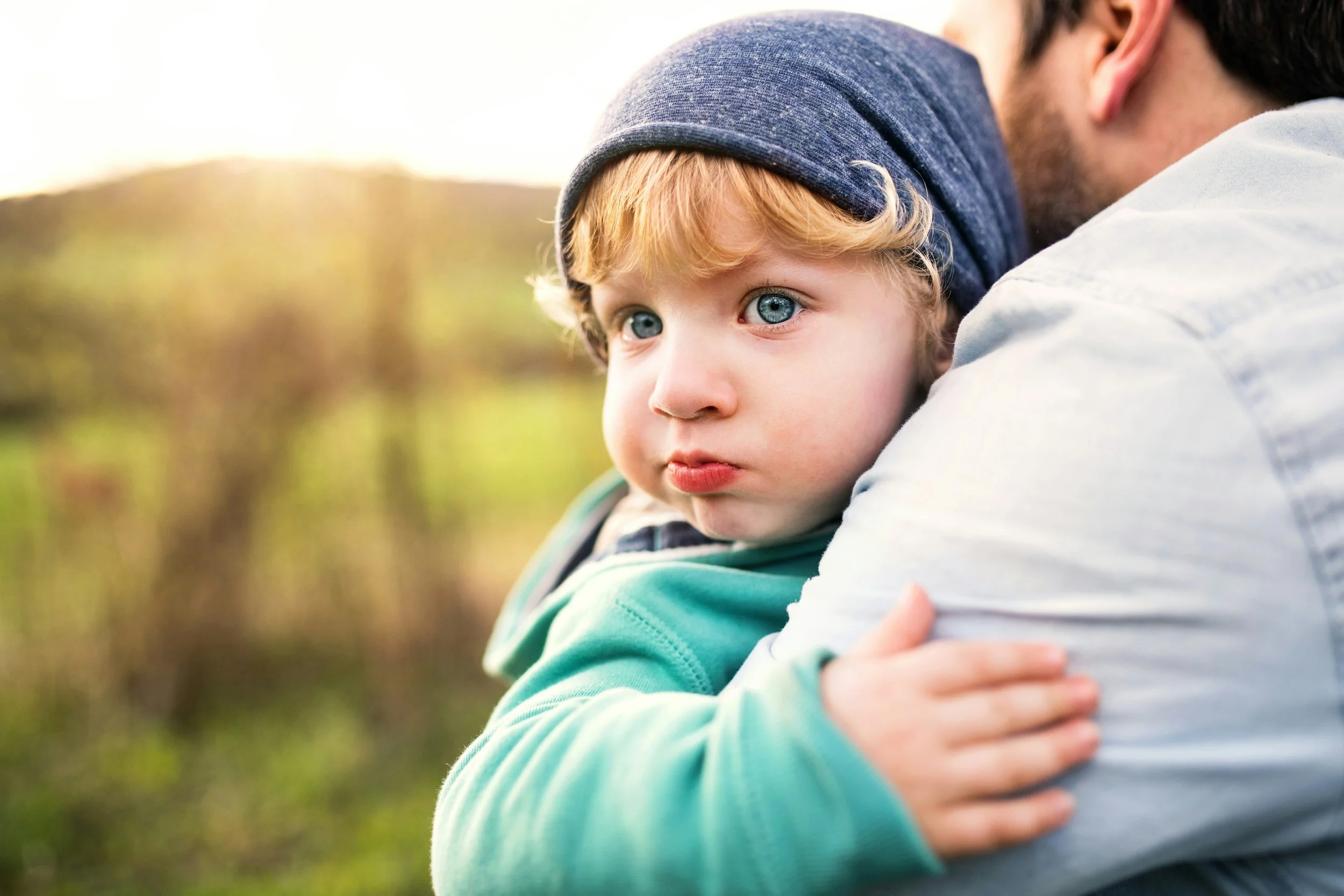 Kind wird im Freien von einer erwachsenen Bezugsperson umarmt, als Symbol für Nähe und Verbindung in der Eltern-Kind-Beziehung.
