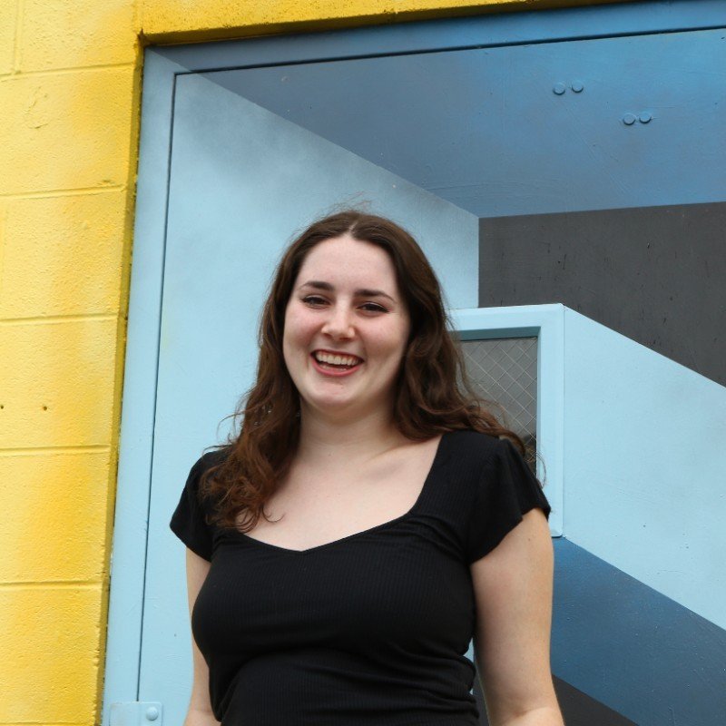 A young woman smiling outdoors in front of a colorful mural.