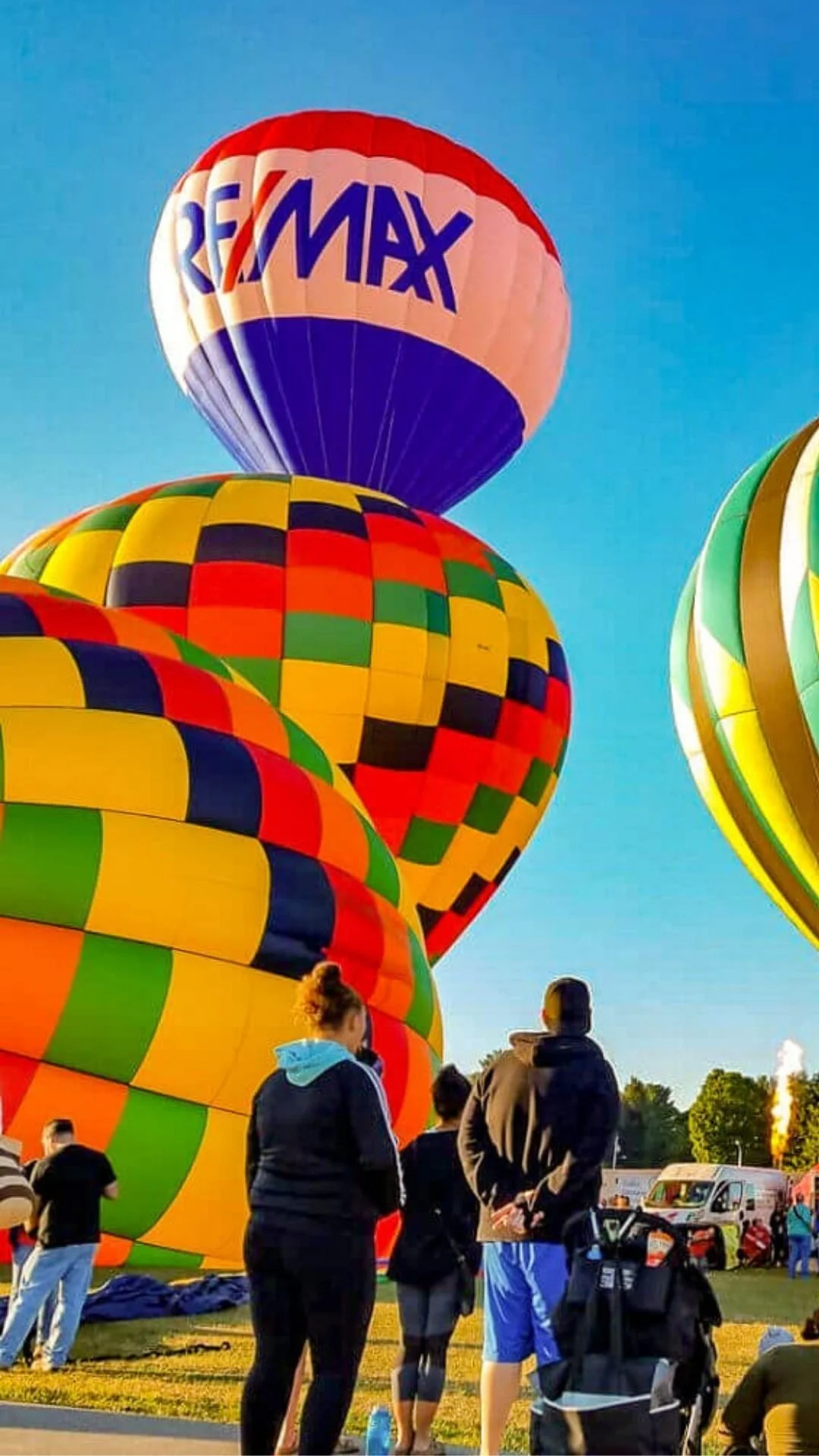 Group of people watching colorful hot air balloons preparing for launch at a festival on a clear day.