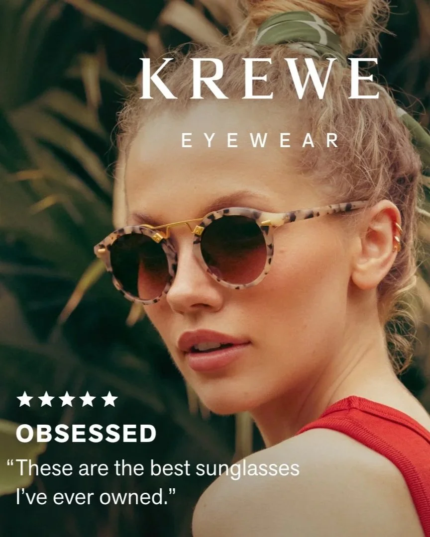 A woman with curly hair tied with a green bandana wearing leopard print sunglasses and a red tank top, standing among green plants, promoting Krewe eyewear.