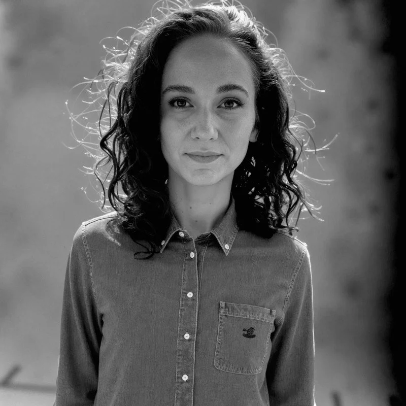 Black and white portrait of a woman with curly hair wearing a denim shirt.