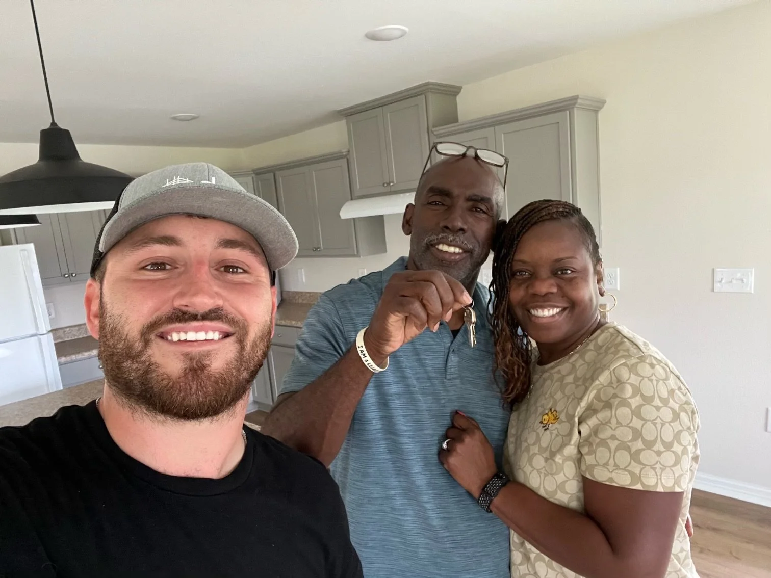Three people smiling and posing together in a kitchen, one holding keys.