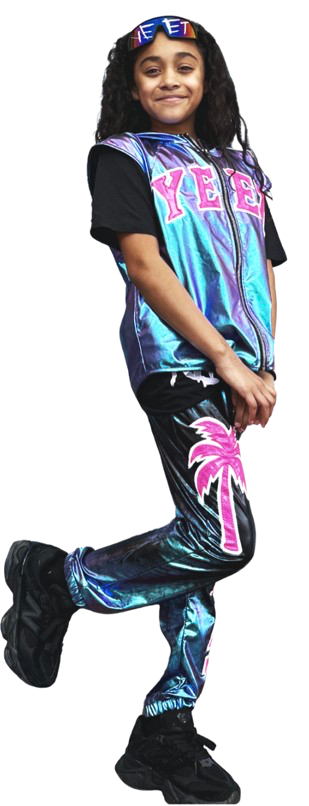 A young girl wearing a colorful 'YEE' vest, black T-shirt, shiny pants with a pink palm tree design, black boots, and a blue headband with the word 'YEE' on it, standing against a white background.