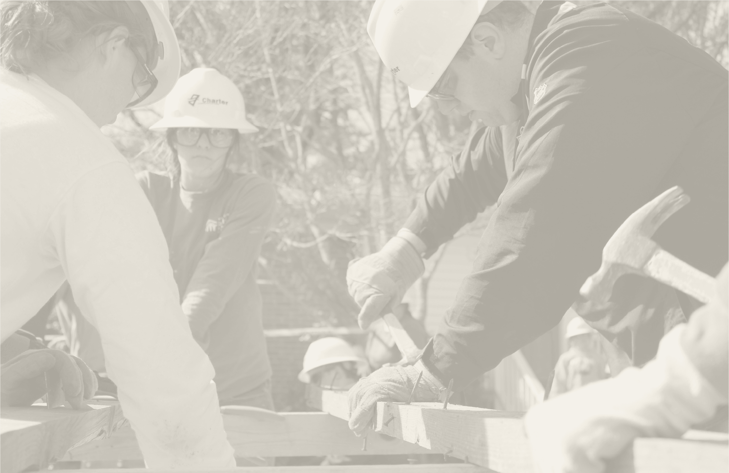 Construction workers wearing safety helmets and glasses working on a wooden structure outdoors.