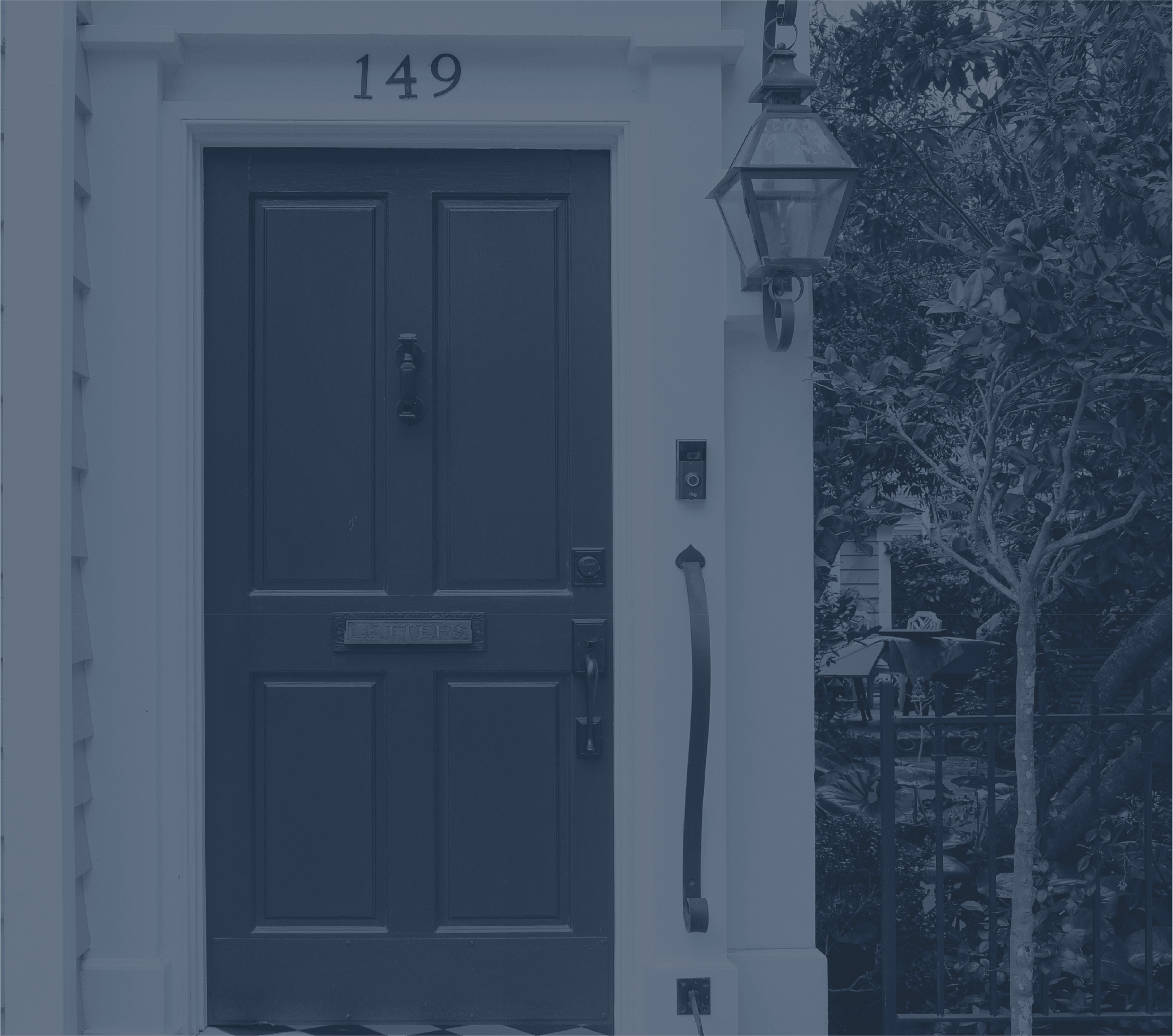 Front door with house number 149, a lantern-style light fixture, and greenery on the side in a residential neighborhood.