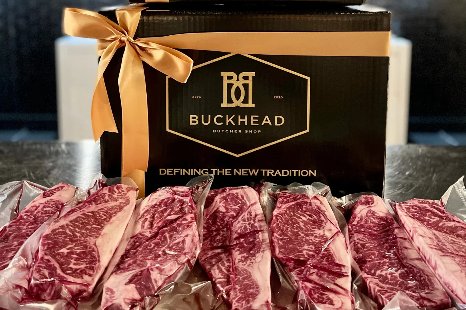 A Buckhead Butcher Shop gift box tied with a gold ribbon, with steaks alongside