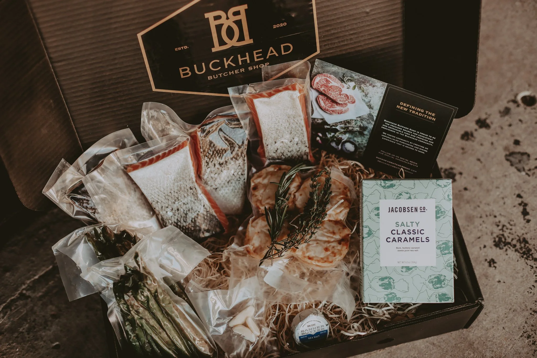 An open gift box packed with vacuum-sealed steaks, fresh herbs and caramels