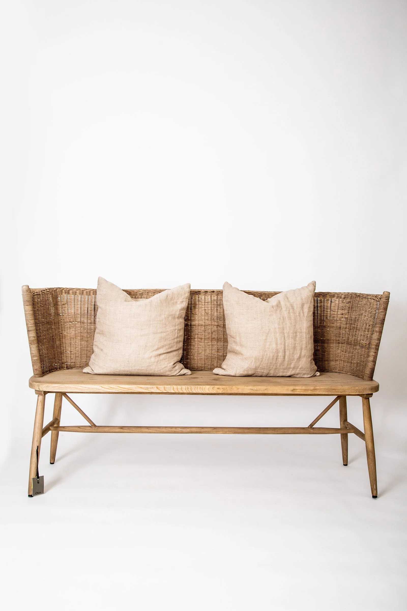 A wooden bench with a woven backrest and legs, adorned with three beige cushions, standing against a plain white background.