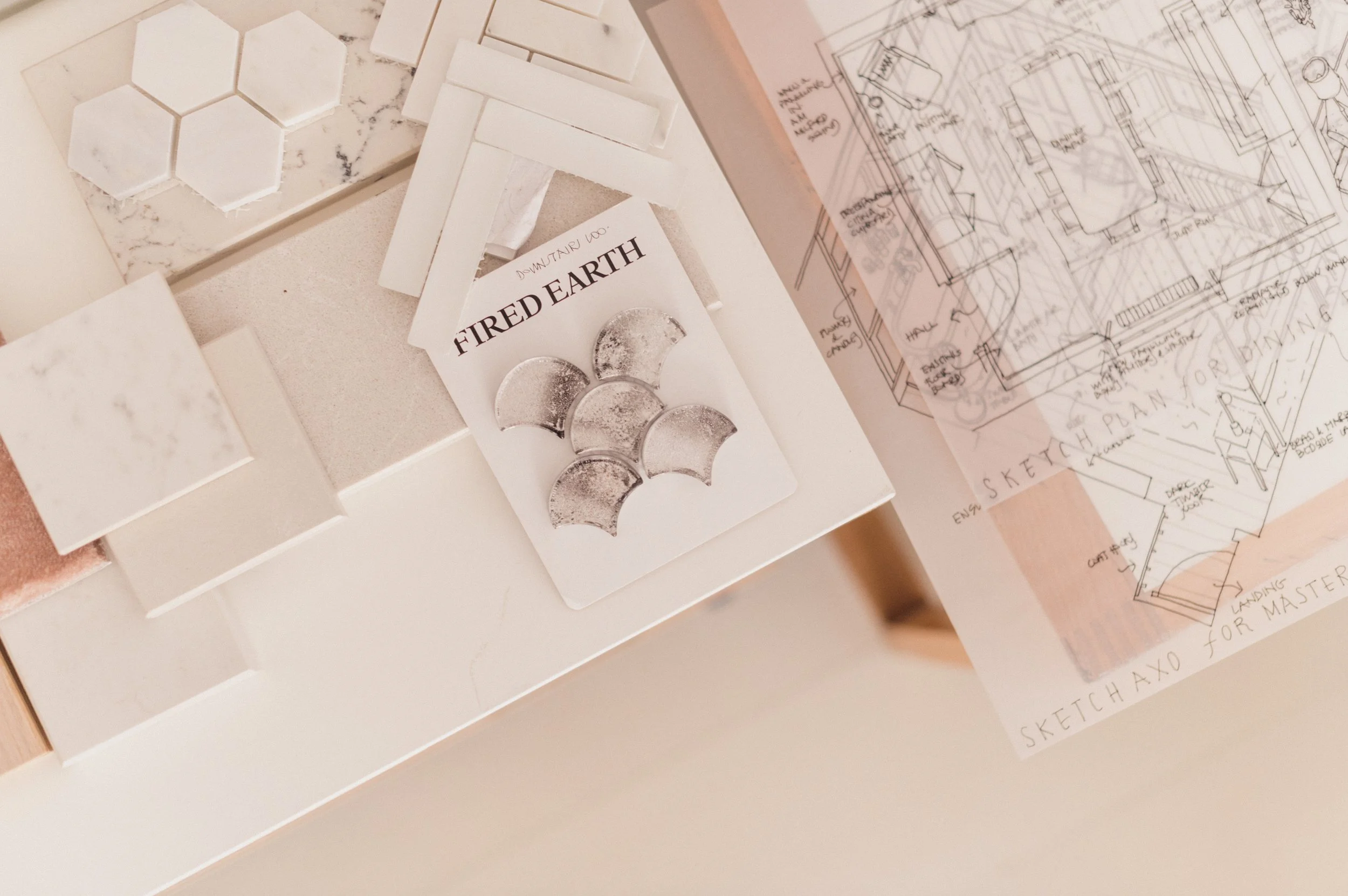 A flat lay of design and craft materials including white tile samples, a sketch, and a label that reads 'DOWNTOWN LOFT FIRED EARTH'.