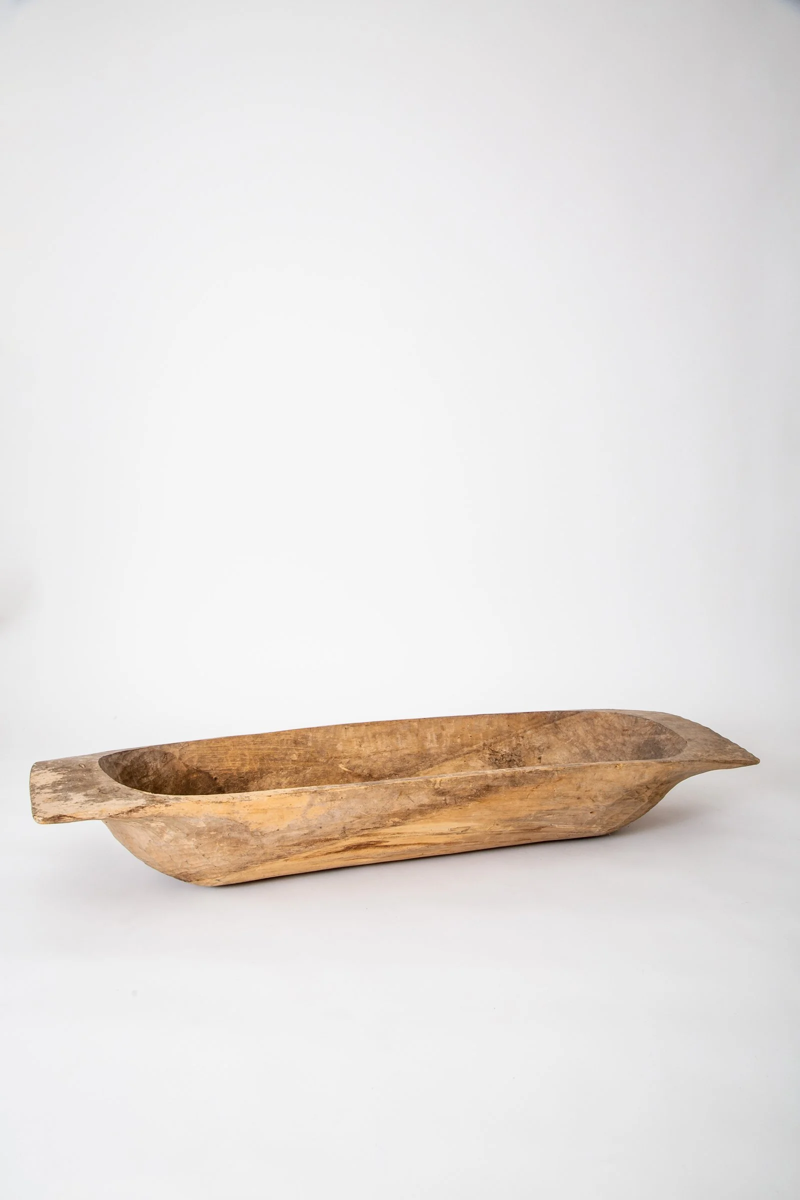 A carved wooden boat-shaped container with a hollowed-out interior, placed on a white surface against a plain white background.