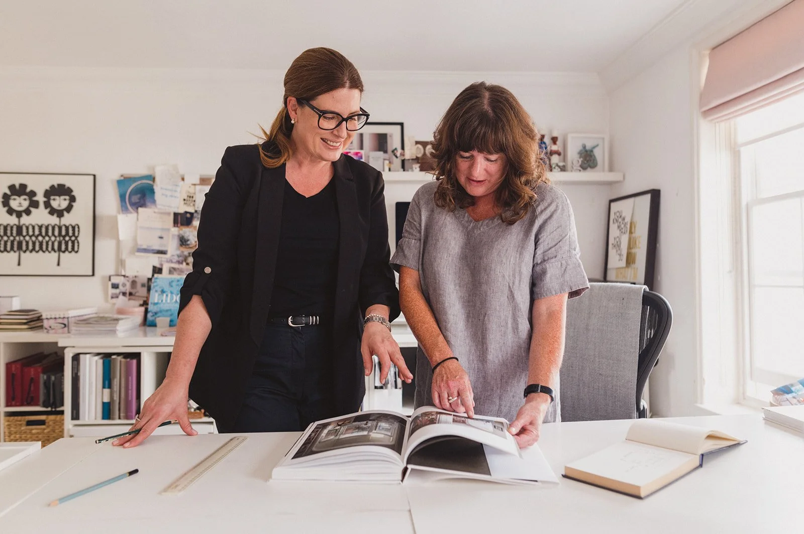 Two women looking at a large photo album together in a bright, organized room.