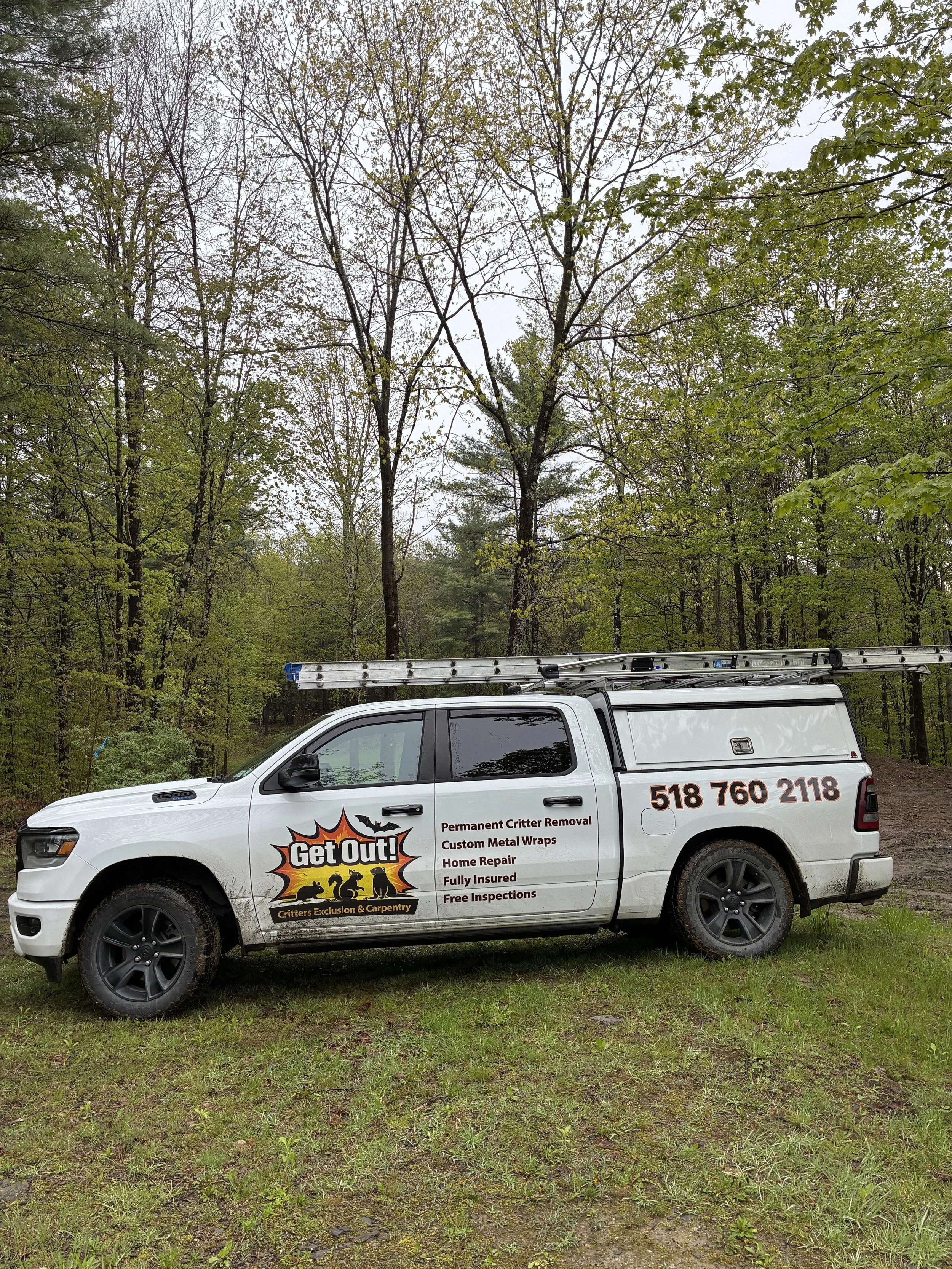 A white pickup truck parked on grass with a ladder on top, showing a logo and contact information for Critters Exclusion & Carpentry, surrounded by trees in a wooded area.